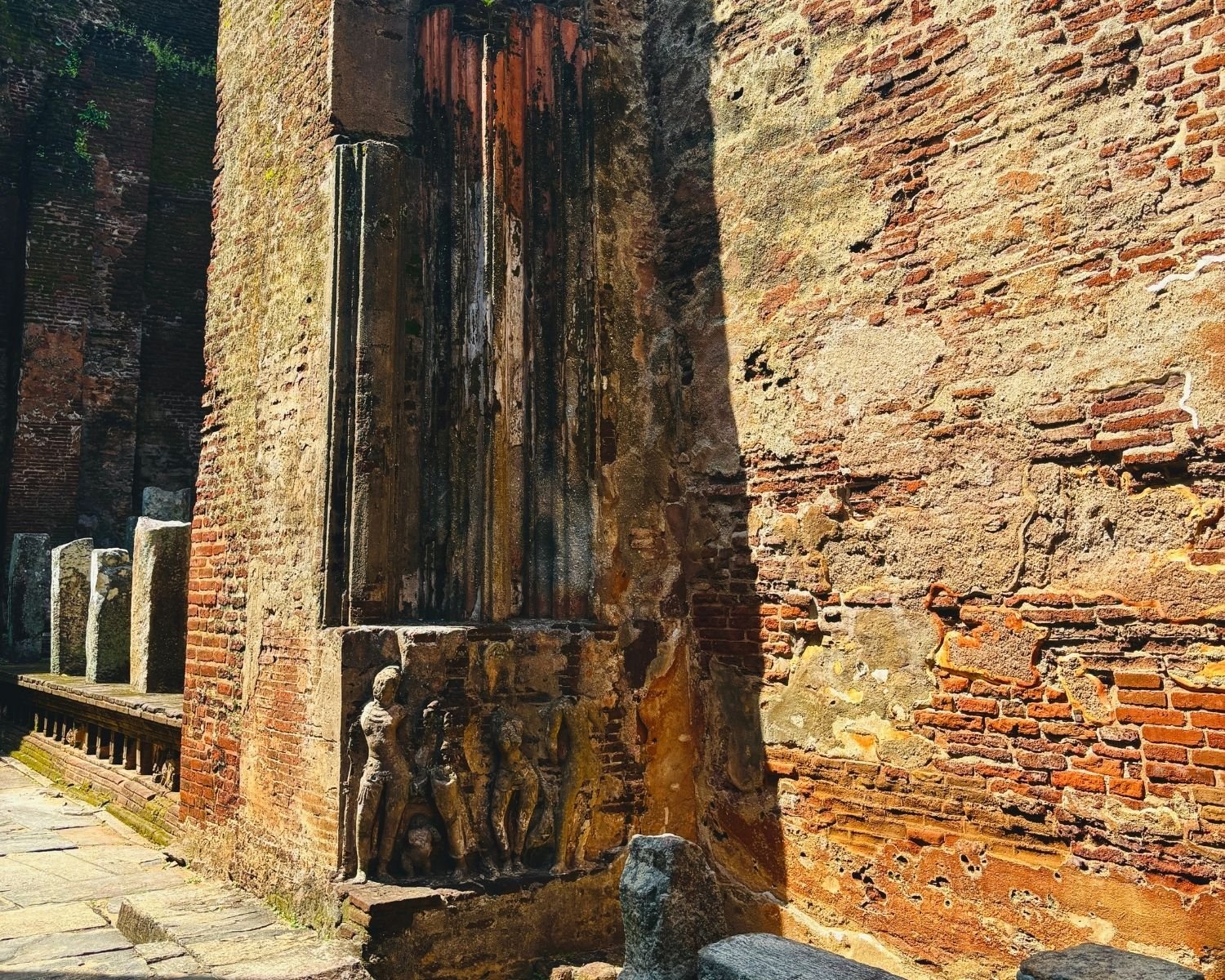 Stucco relief figures on weathered brick wall inside Lankatilaka with sunlight and shadows