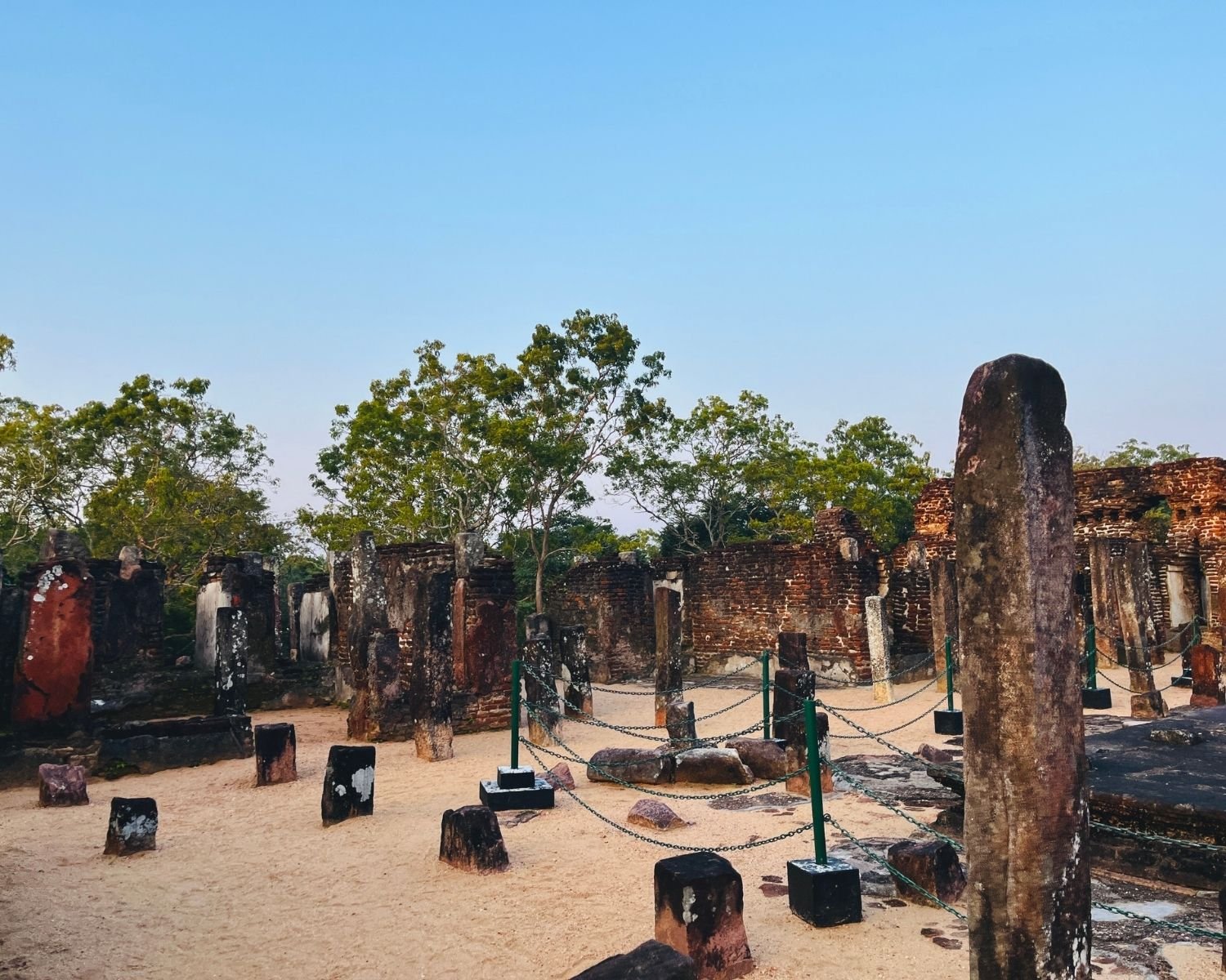 Stone pillars and brick ruins inside Baddhasima Prasadaya with sand floor at dusk