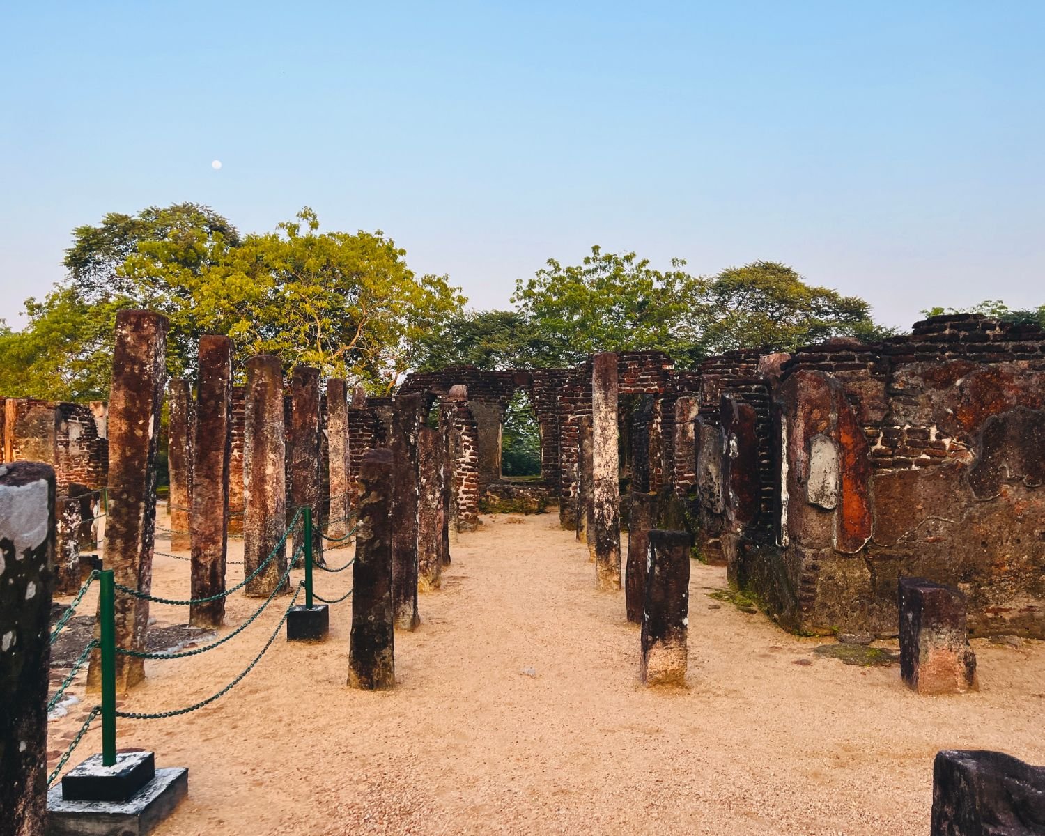 Stone pillars and arched window inside Baddhasima Prasadaya with sand floor at dusk