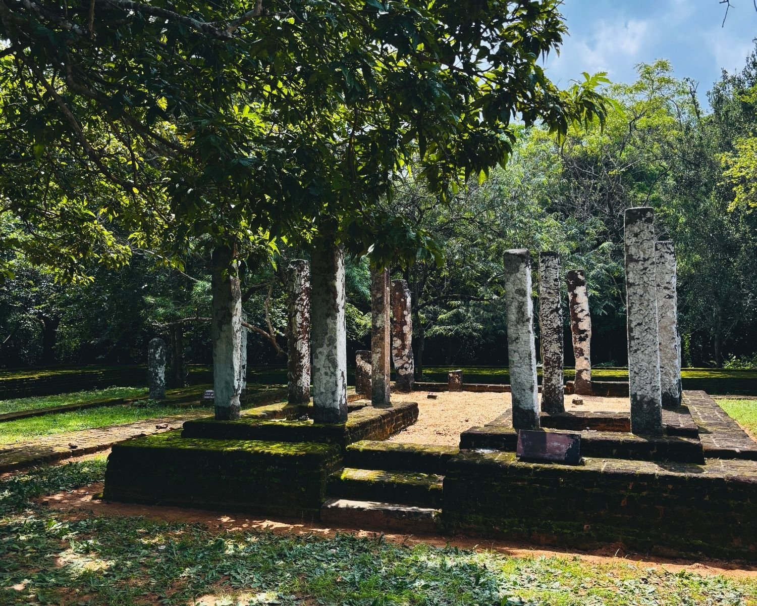 Shaded residential cell remains at Potgul Vihara with standing stone pillars and brick foundations
