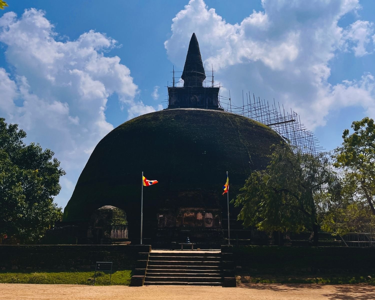 Large dome of Rankoth Vehera stupa with tall spire, Buddhist flags, and stone steps at Alahana Pirivena