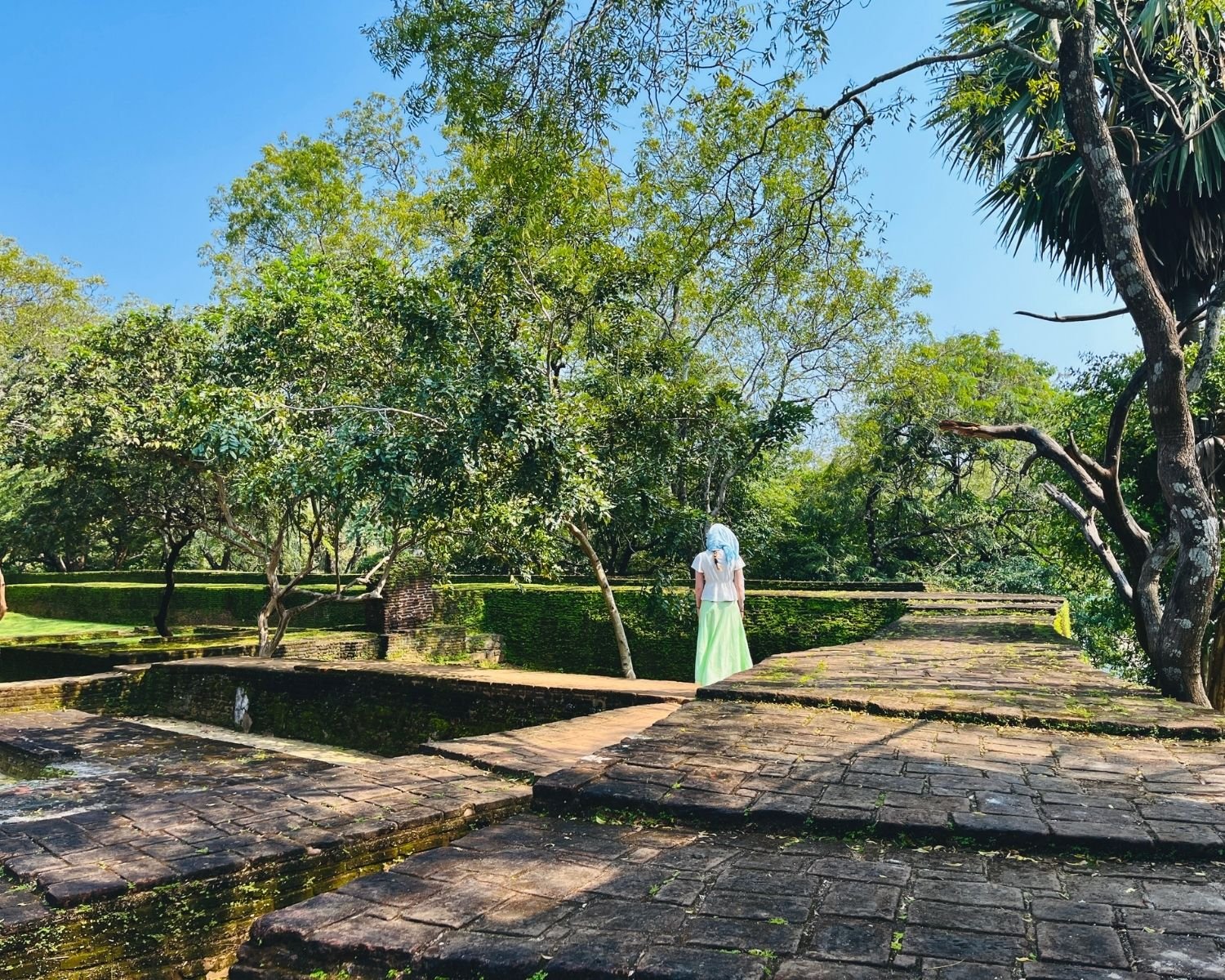 Thick brick walls and layered foundation remains in Royal Palace Complex with main palace visible through trees