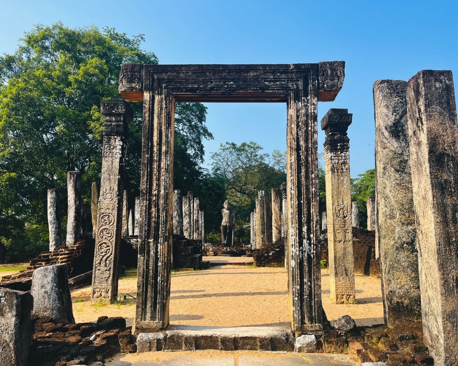 Carved stone doorway of Atadage framing standing Buddha statue between ornate pillars