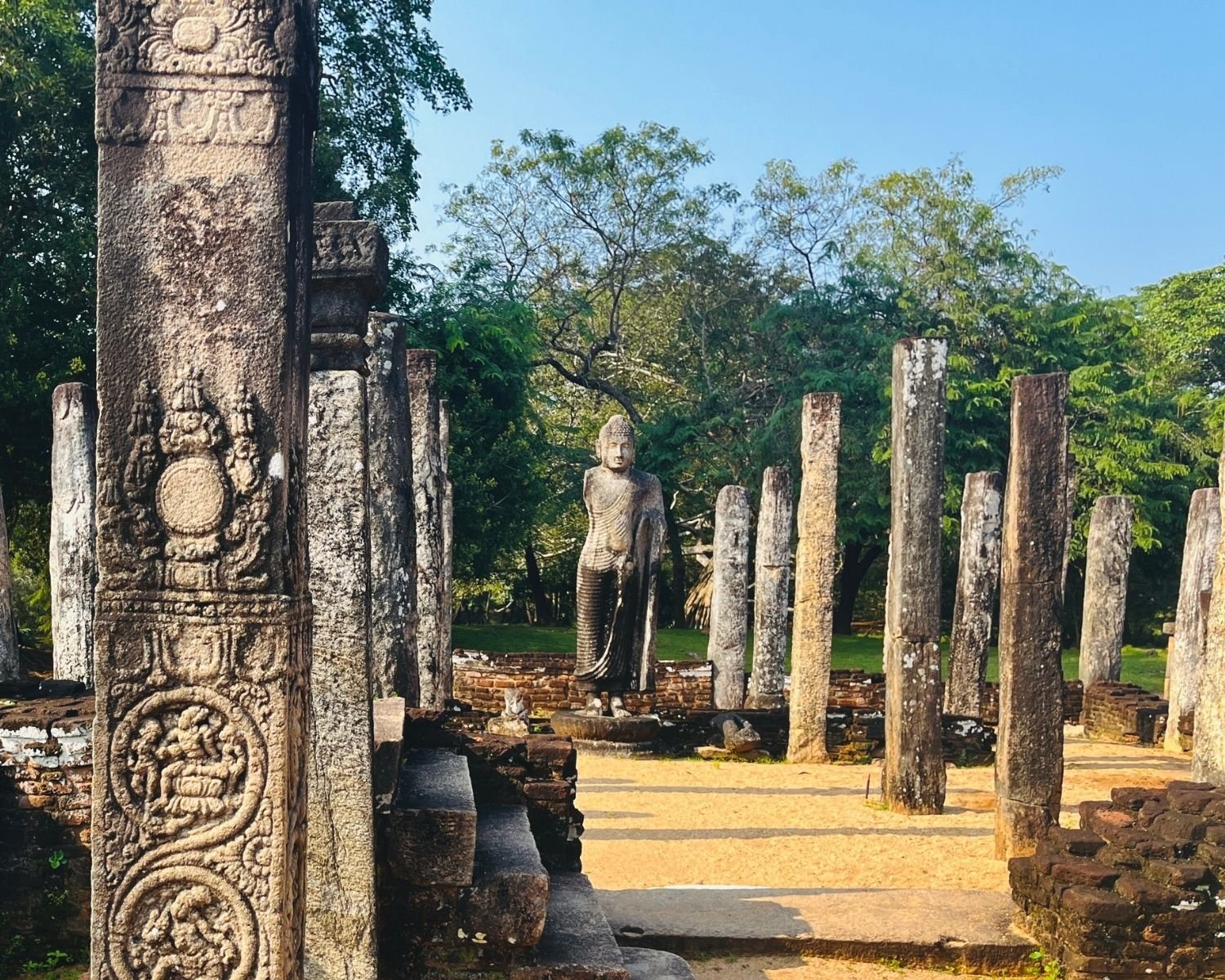 Ornate carved stone pillar with medallion reliefs in Atadage with Buddha statue beyond