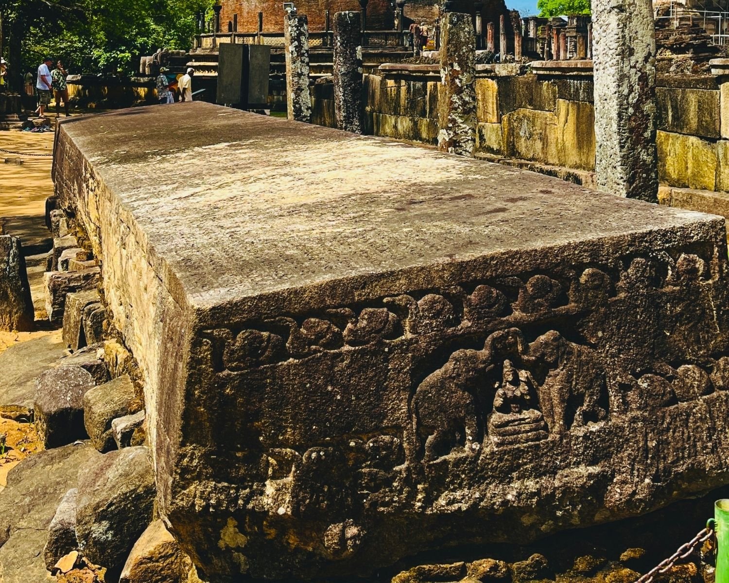 Angled view of Gal Potha showing carved elephant panel, inscription surface, and Vatadageya ruins behind