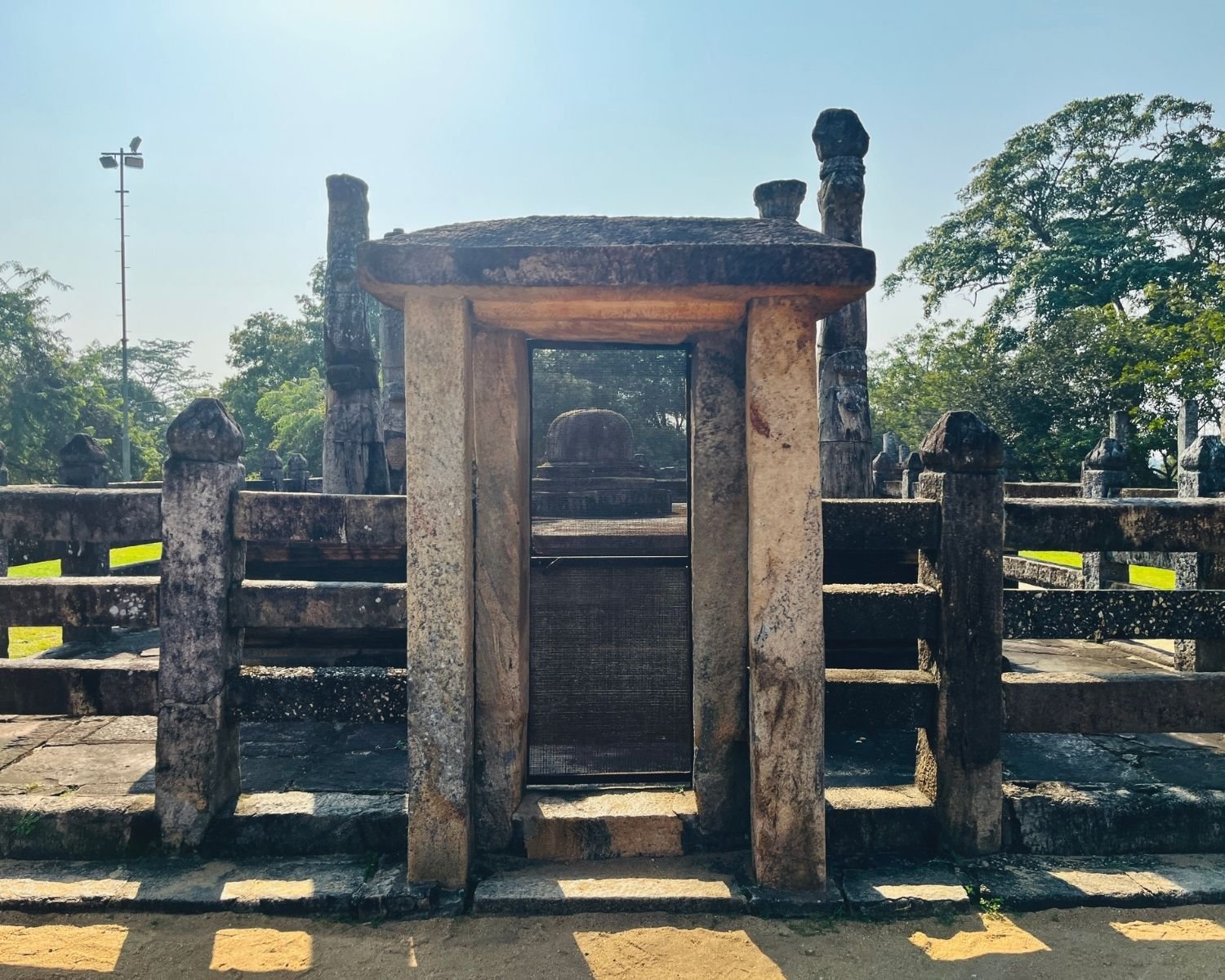 Open stone doorway through vedika railing of Nissanka Latha Mandapaya with stupa base and pillars beyond
