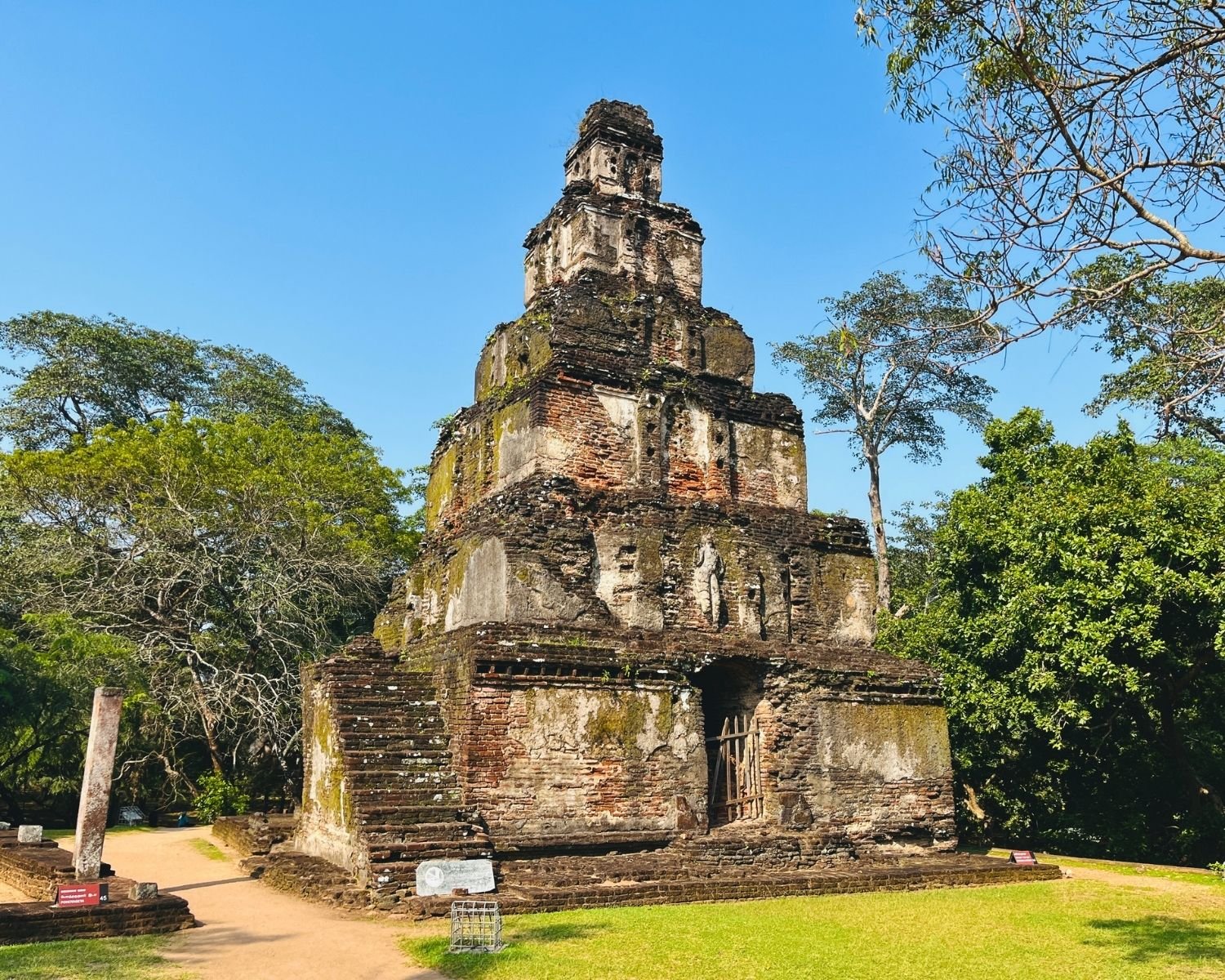 Angled view of Satmahal Prasada seven-tiered brick pyramid with gated doorway and stone pillar