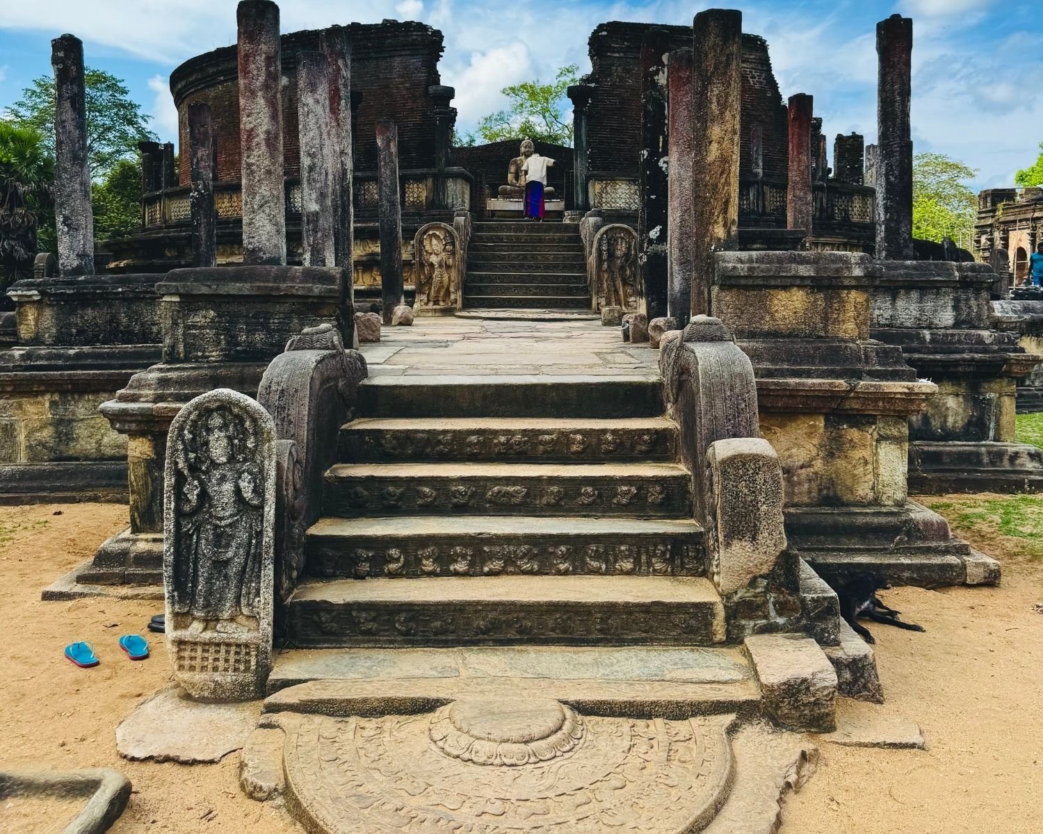 Wide front view of Vatadage with circular brick walls, stone pillars, guard stones, and visitor
