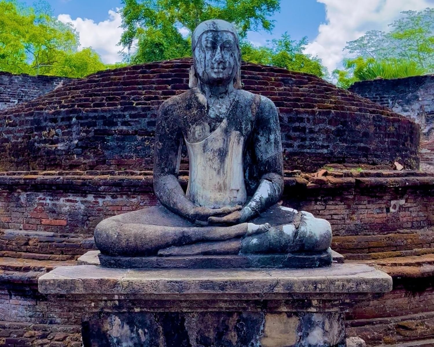 Vatadage tiered brick stupa dome with moss, seated Buddha, and stone pillars