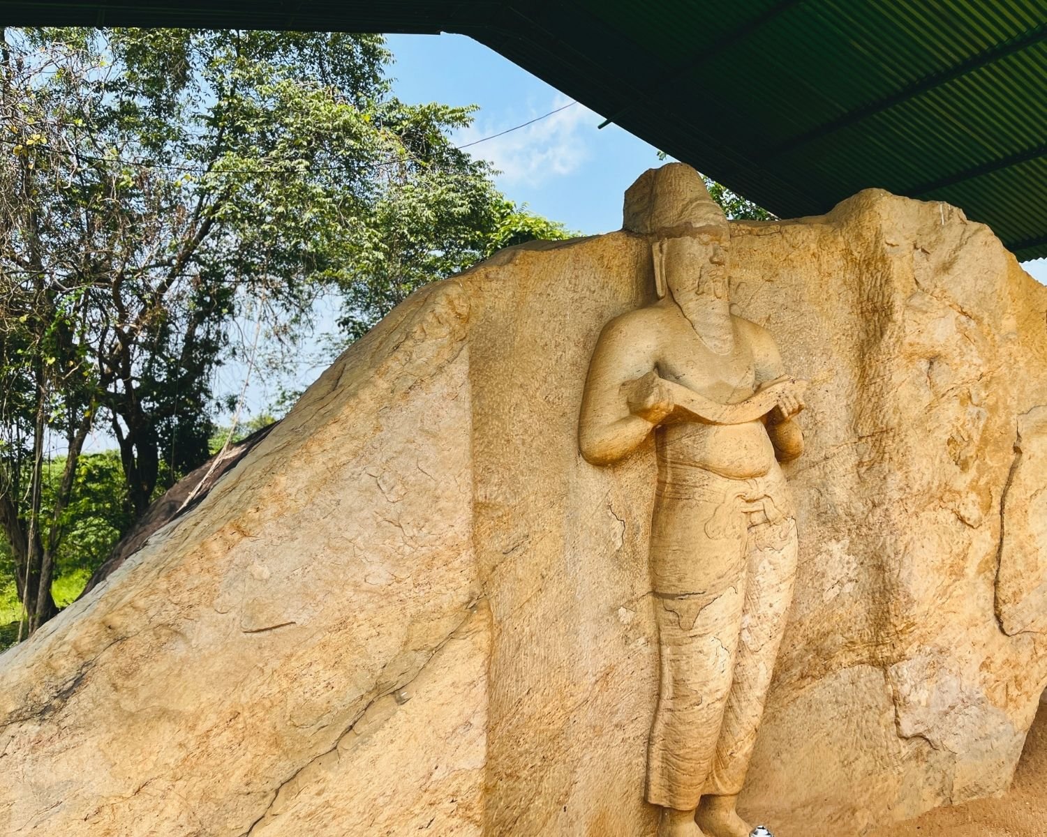 Side view of statue traditionally identified as King Parakramabahu I beside natural stone surface