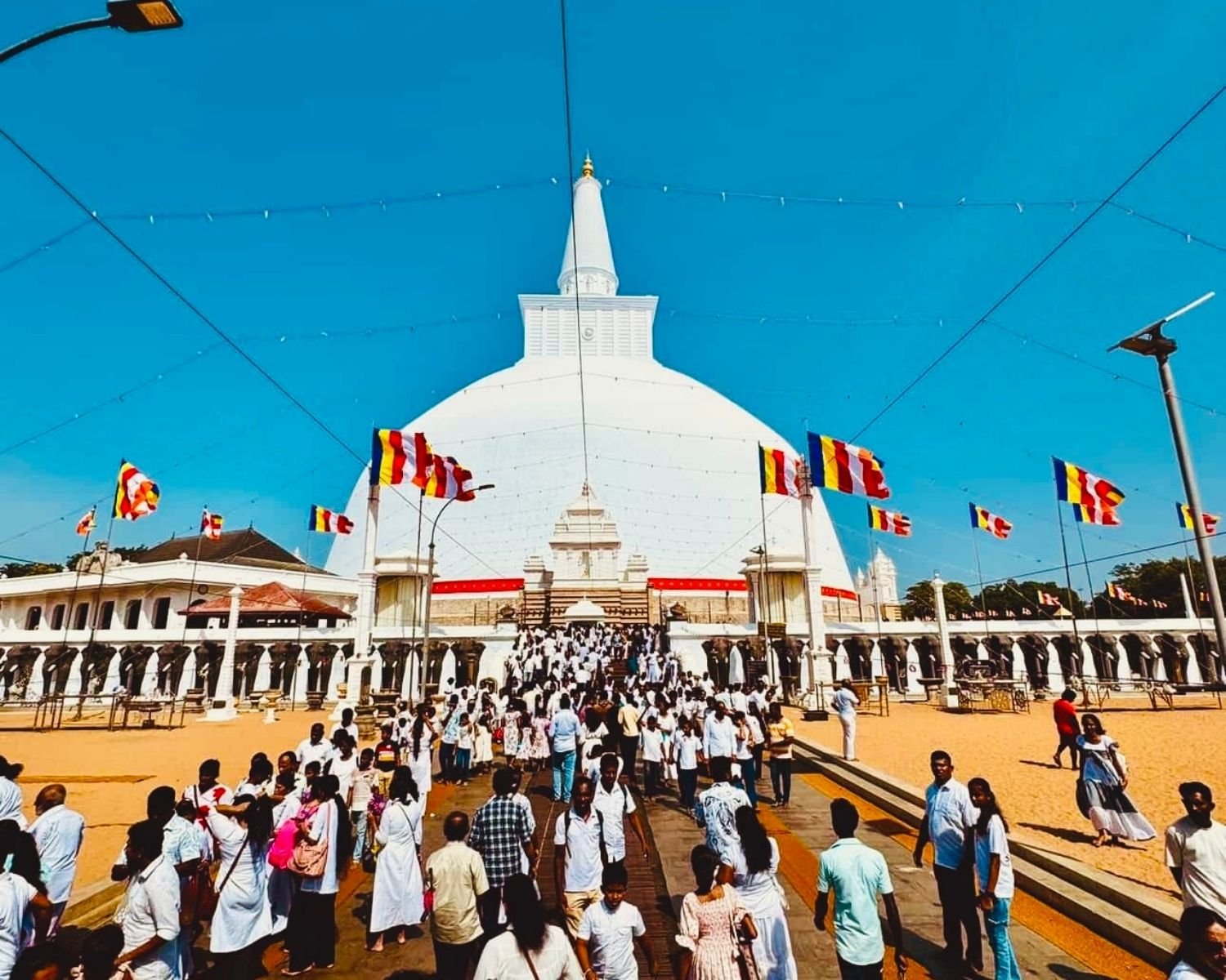 Ruwanwelisaya stupa east approach path with Buddhist flags and pilgrims on Poya day