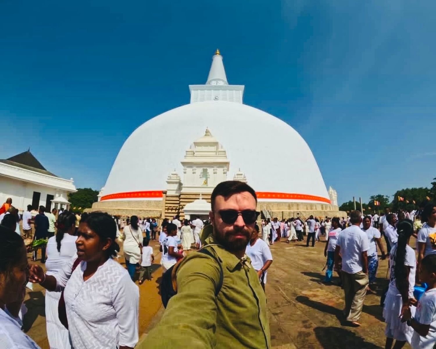 Traveler selfie at Ruwanwelisaya east maluwa with full stupa dome and crowd of devotees on Poya day