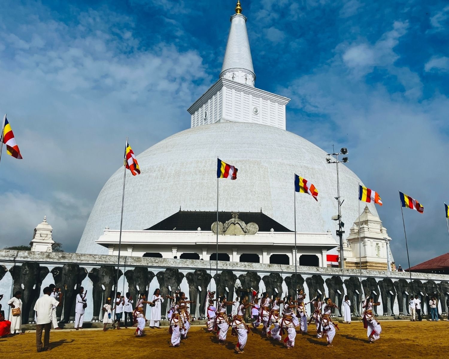 Kandyan dancers performing in front of Ruwanwelisaya stupa elephant wall with Buddhist flags