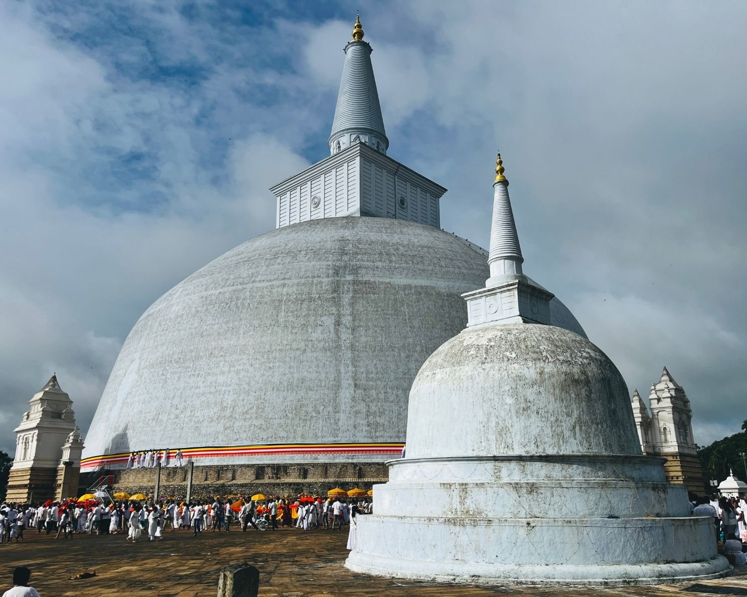 Ruwanwelisaya main stupa with smaller satellite stupa from northeast with pilgrims and yellow umbrellas