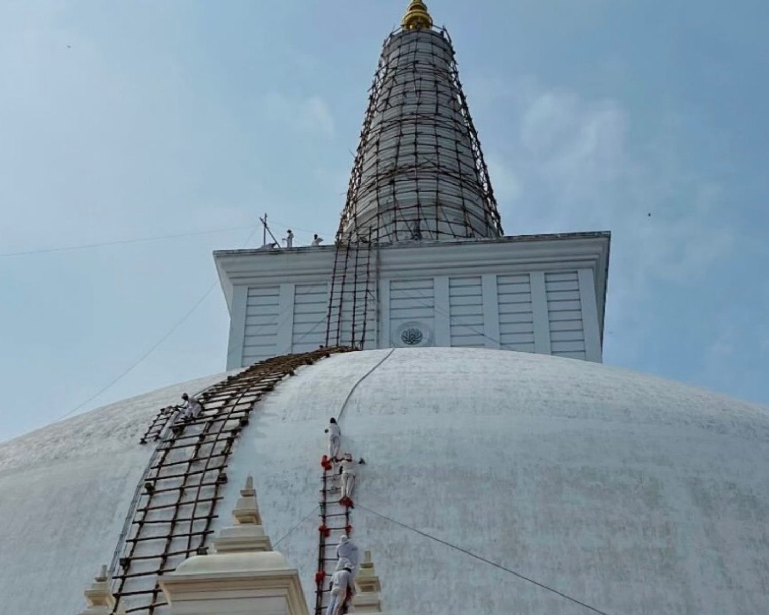 Devotees performing Piyum Pooja painting ceremony on Ruwanwelisaya stupa dome with bamboo ladders