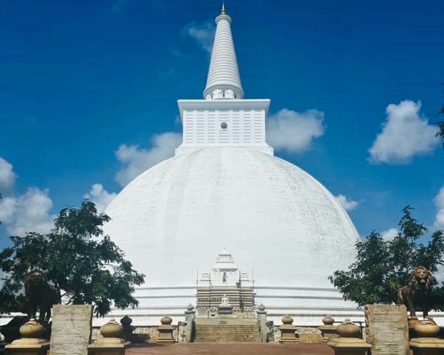 Full front view of Sandahiru Seya white stupa in Anuradhapura with square harmika, spire, stone steps, and lion statues