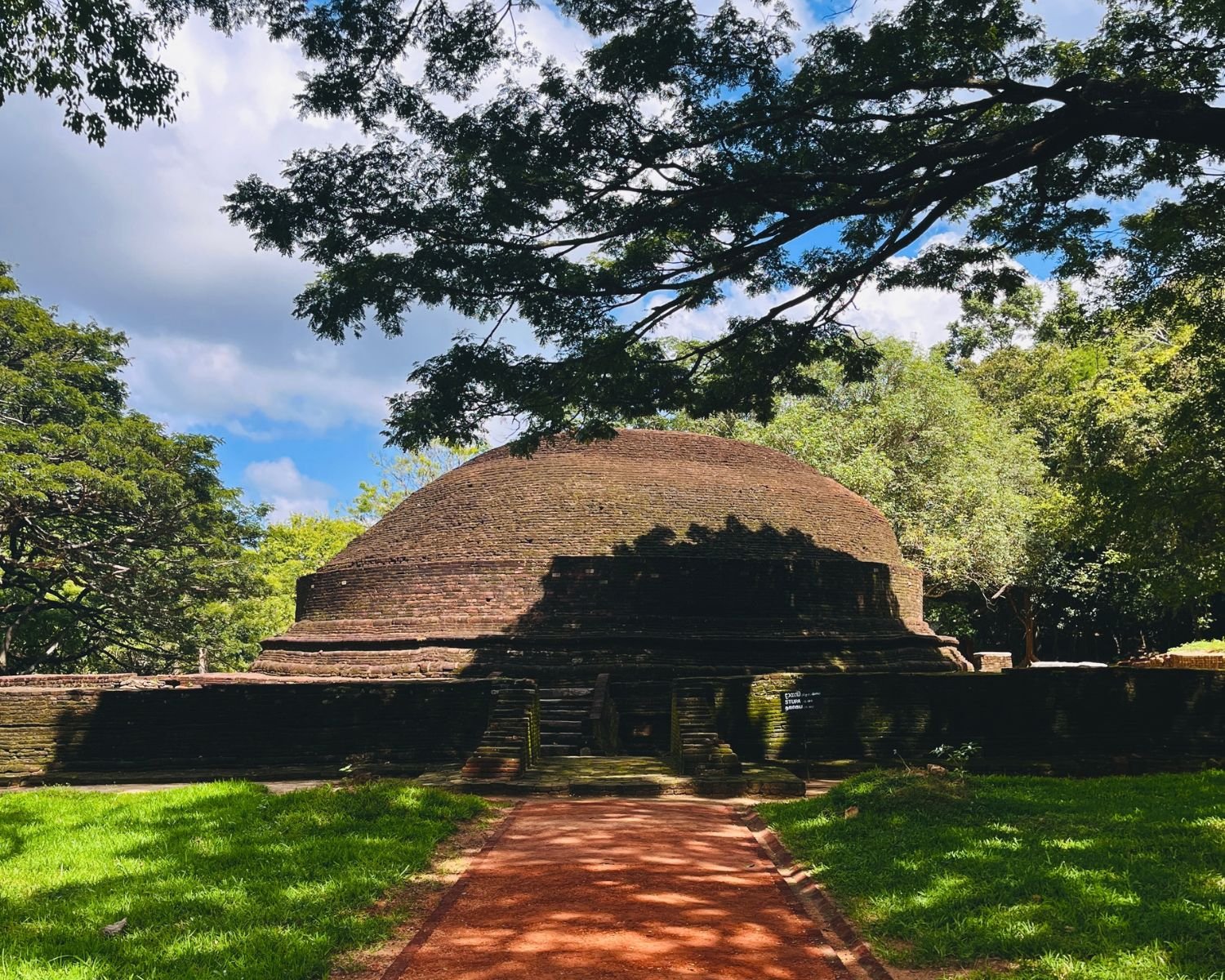 Ancient brick dagaba surrounded by forest and a red earth pathway