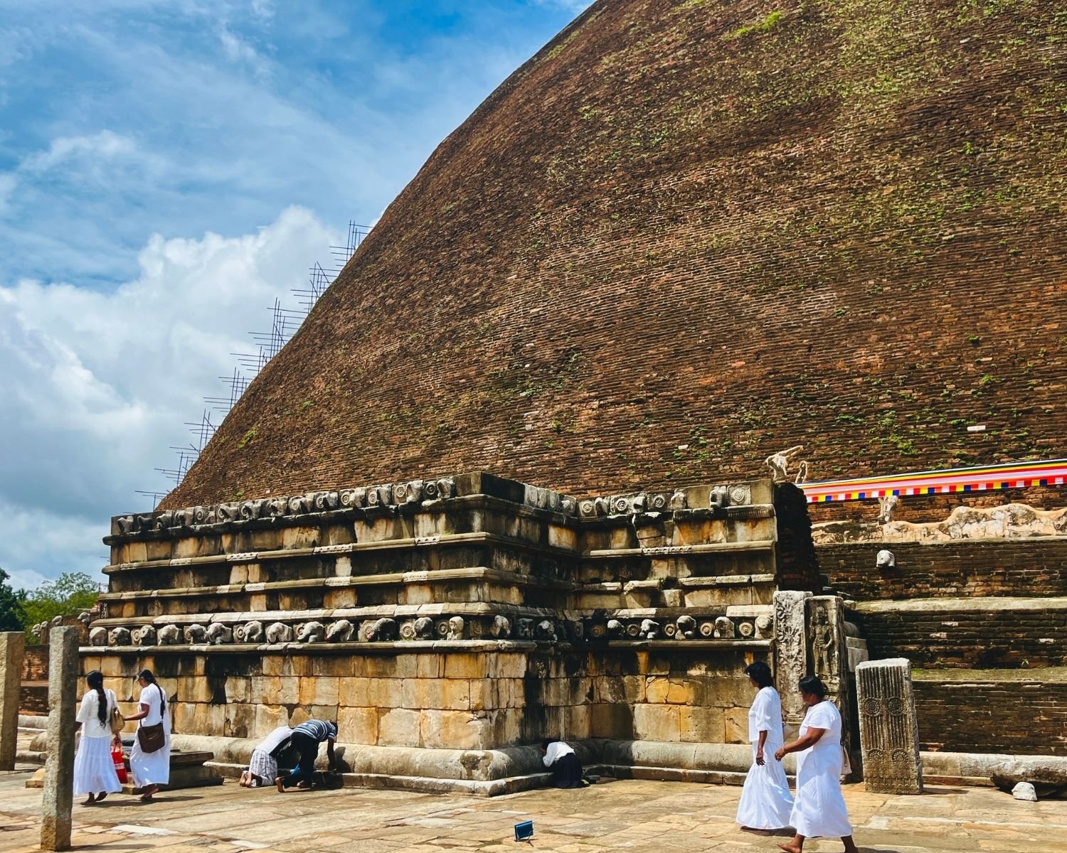 East wahalkada at Abhayagiri Stupa with carved elephant frieze, layered stone base, guardstone and fluted pillar, massive brick dome rising behind with bamboo scaffolding in Anuradhapura