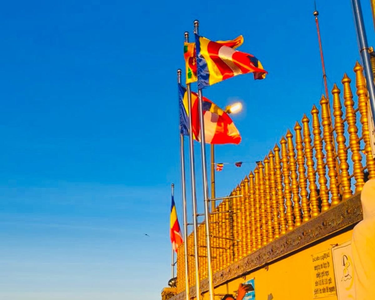Buddhist flags and Sri Lankan flag fly above gold railing at Adams Peak Sri Pada summit shrine under clear blue morning sky