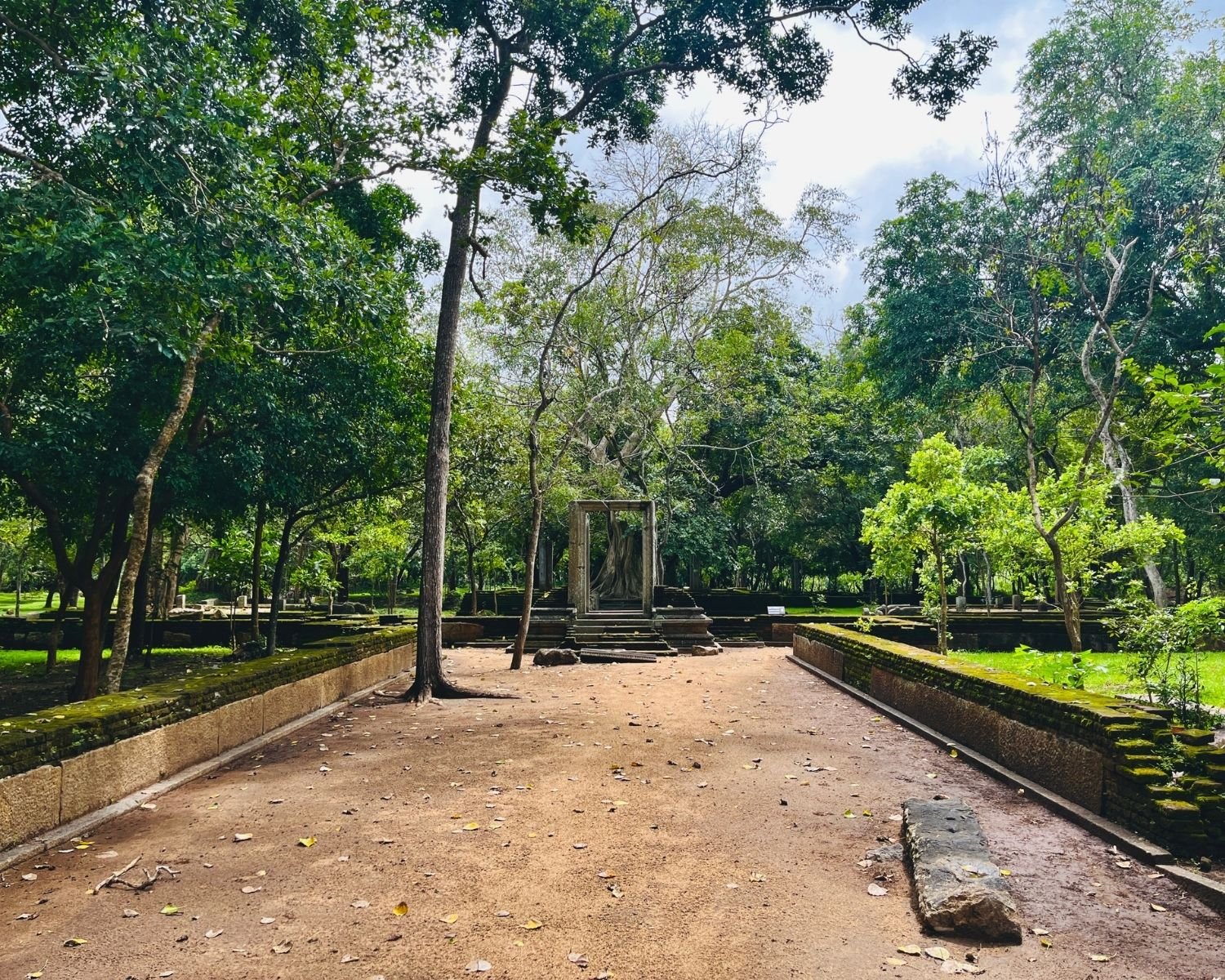 Mystical sand path lined with mossy walls leads to the west stone doorway framing a fairy-tale banyan tree at Abhayagiri Banyan Tree Shrine Anuradhapura