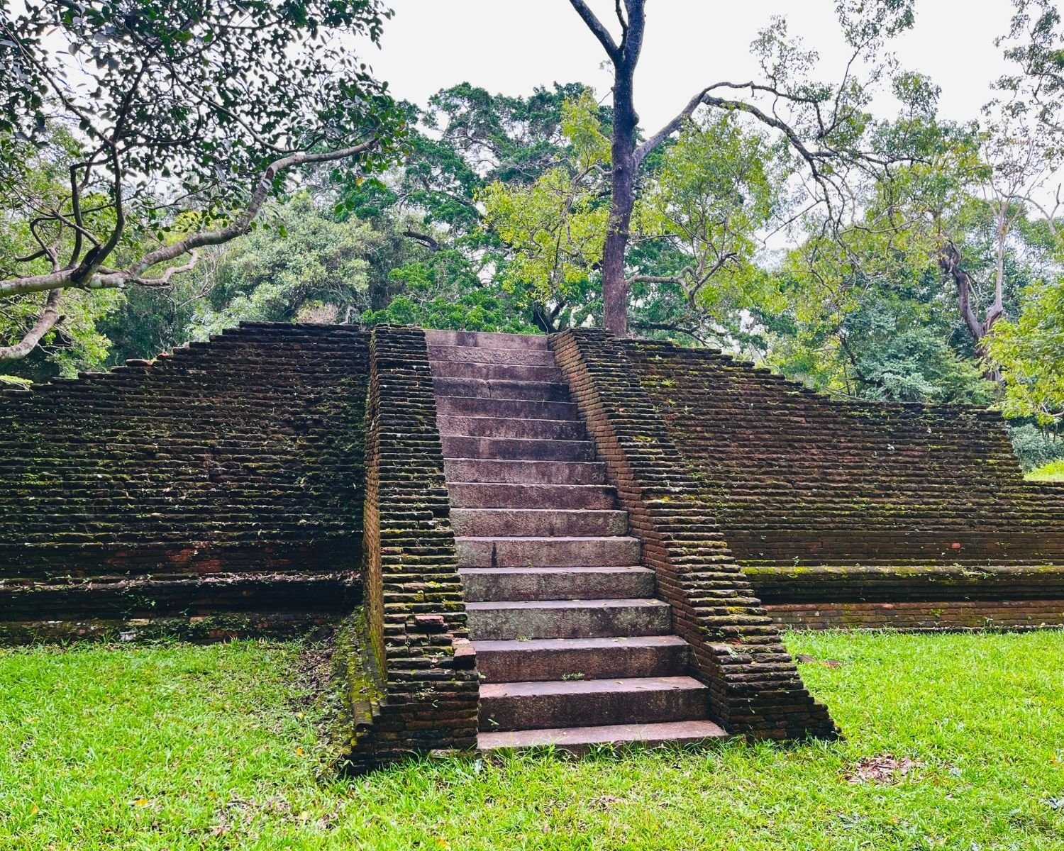 Stone staircase with mossy brick wing walls climbs to the grassy top of Dharani House platform in the eastern monastery complex at Abhayagiri in Anuradhapura