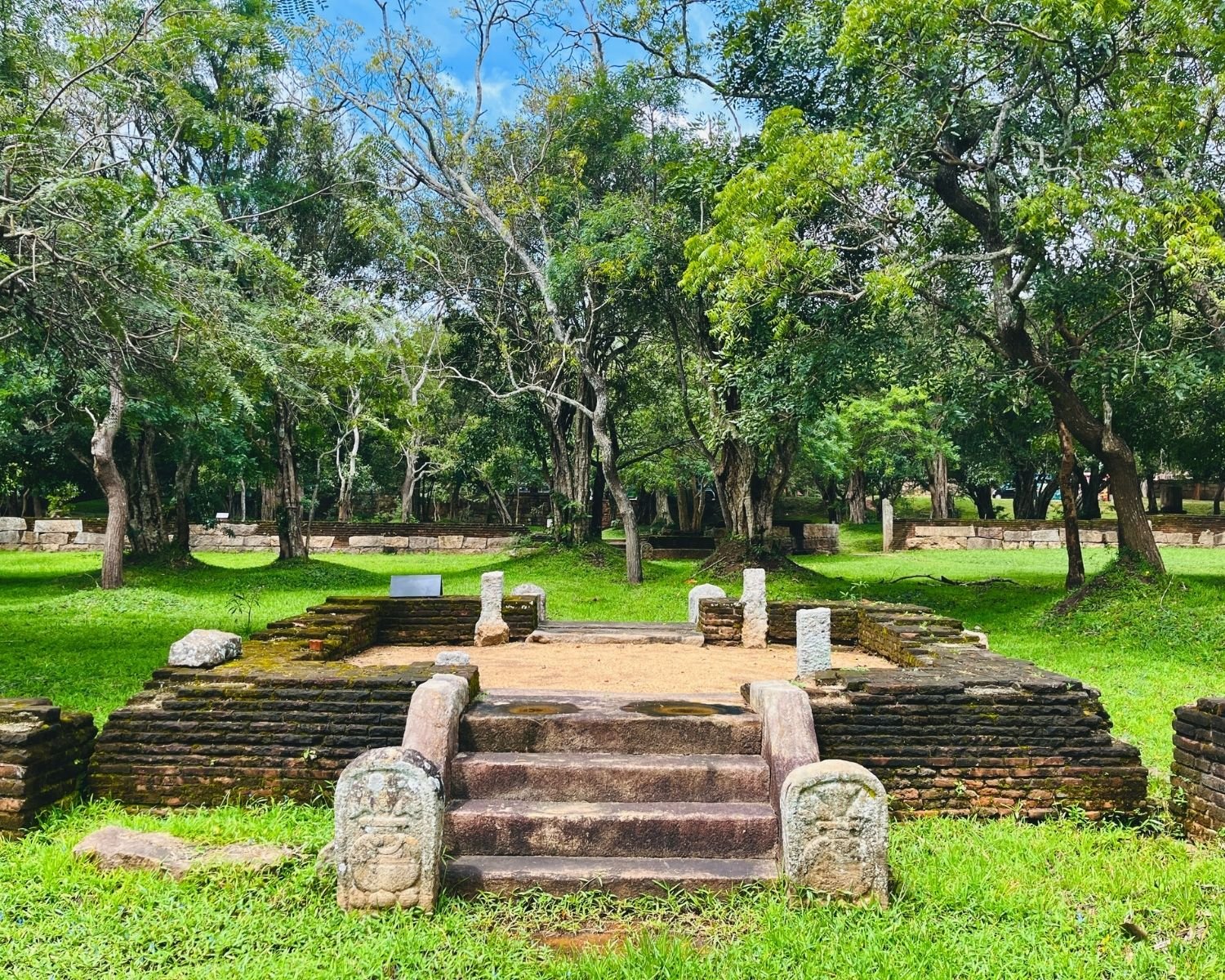 Square brick platform with carved guardstones and stone steps rises from grass in the residential complex at Abhayagiri monastery in Anuradhapura