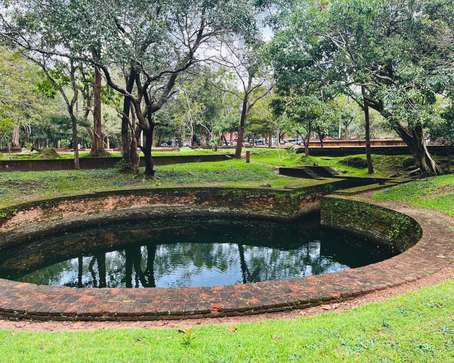 Circular brick pond with narrow channel forming Yaturu Pokuna, the Keyhole Pond, surrounded by grass and trees near Abhayagiri monastery in Anuradhapura