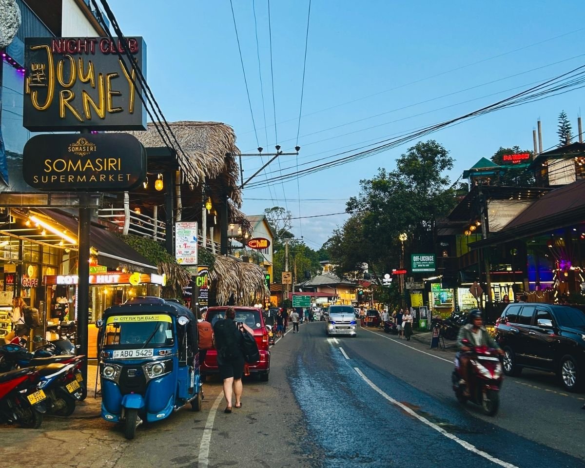 Main street of Ella lined with cafes, restaurants, and tuk tuks at dusk