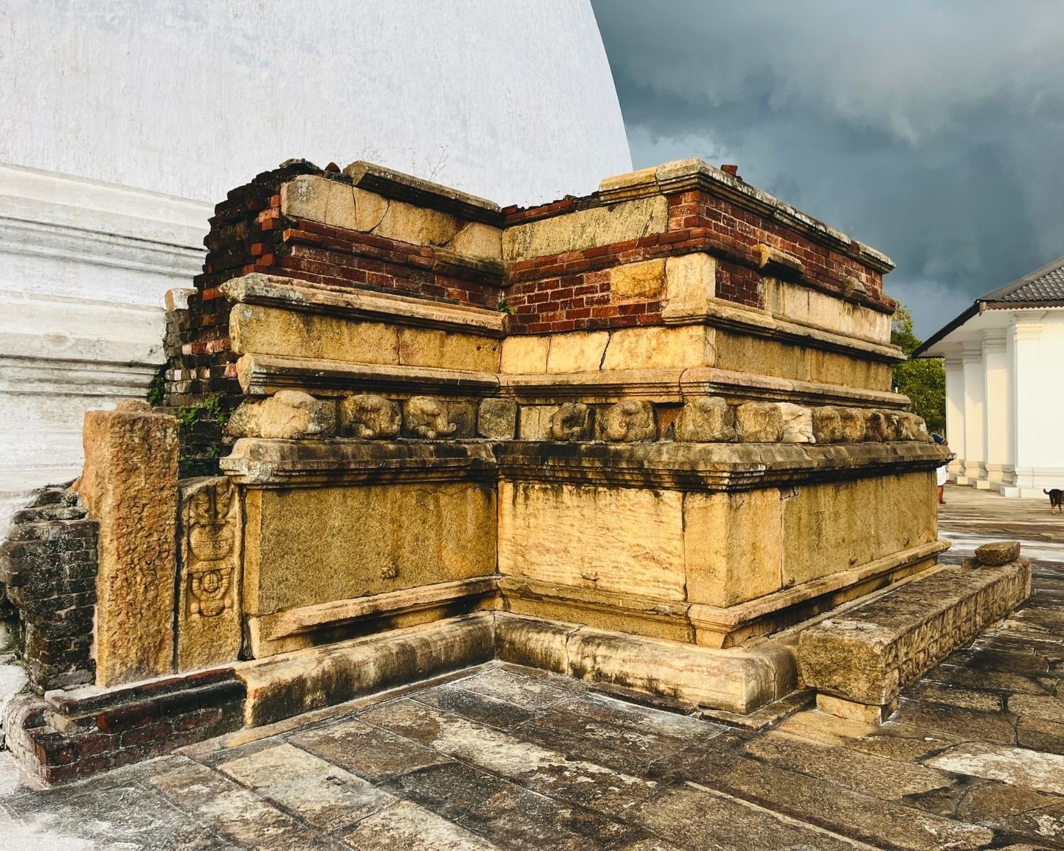 Mirisawetiya Stupa south vahaalkada ancient brick and stone structure with elephant frieze carvings, guardstone relief, wet stone platform, white dome and dark rain clouds at Anuradhapura