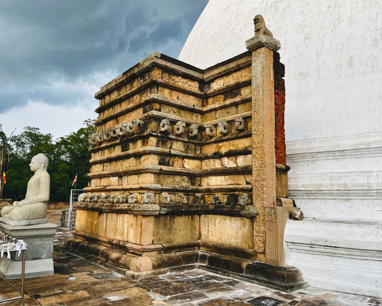 Mirisawetiya Stupa ancient west vahaalkada with elephant frieze, gajasimha and makara brackets, lion capital pillar, Buddha statue in meditation and wet stone platform under cloudy sky at Anuradhapura