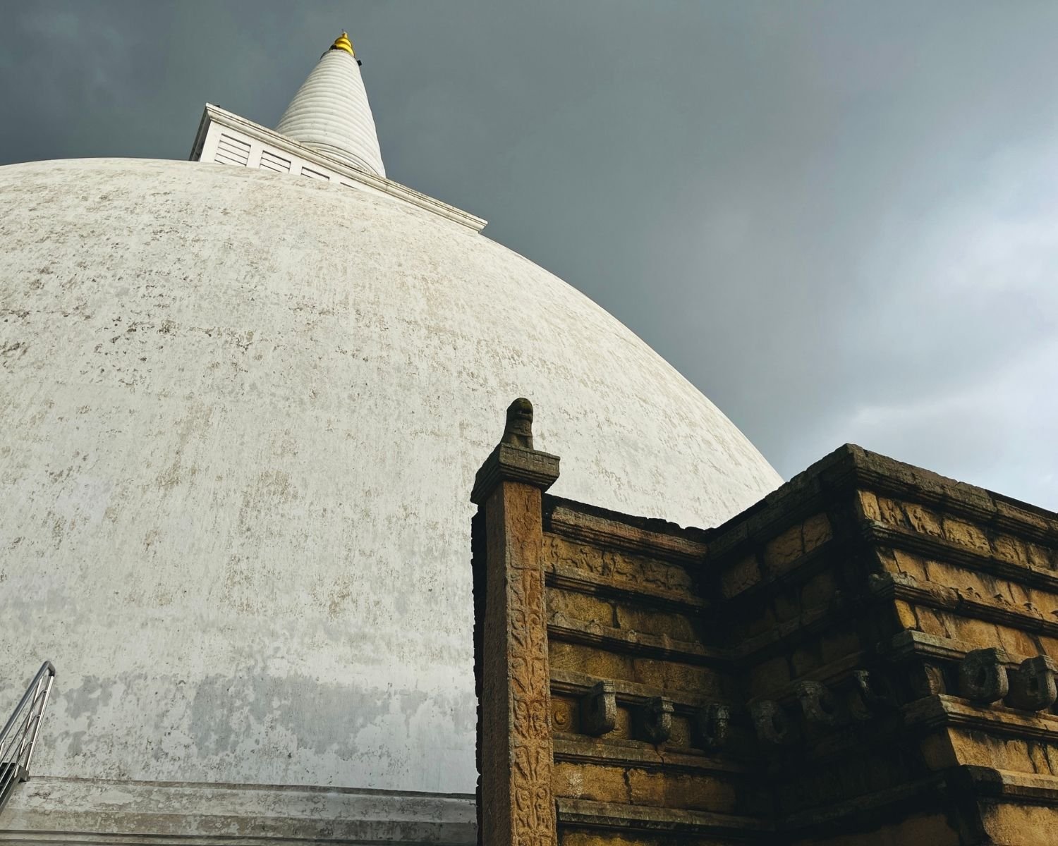 Mirisawetiya Stupa west vahaalkada ancient brick and stone structure with lion capital pillar and carved pilaster, massive white dome with golden kotha pinnacle rising into cloudy sky at Anuradhapura