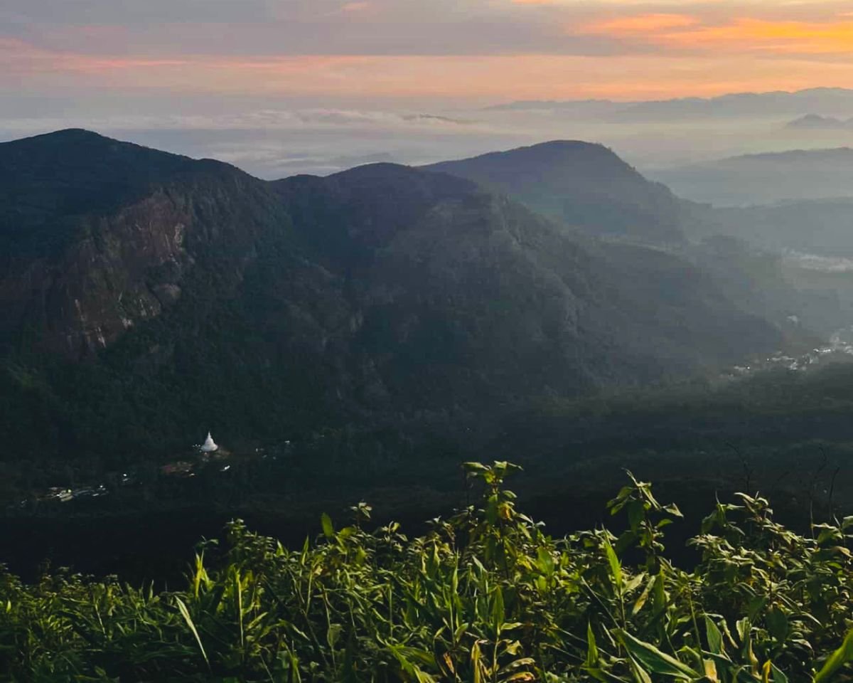Twilight dawn from Point of Needles Indi Katupana on Adams Peak over Peak Wilderness with orange sky Sri Pada cliff and distant Peace Pagoda Nallathanniya