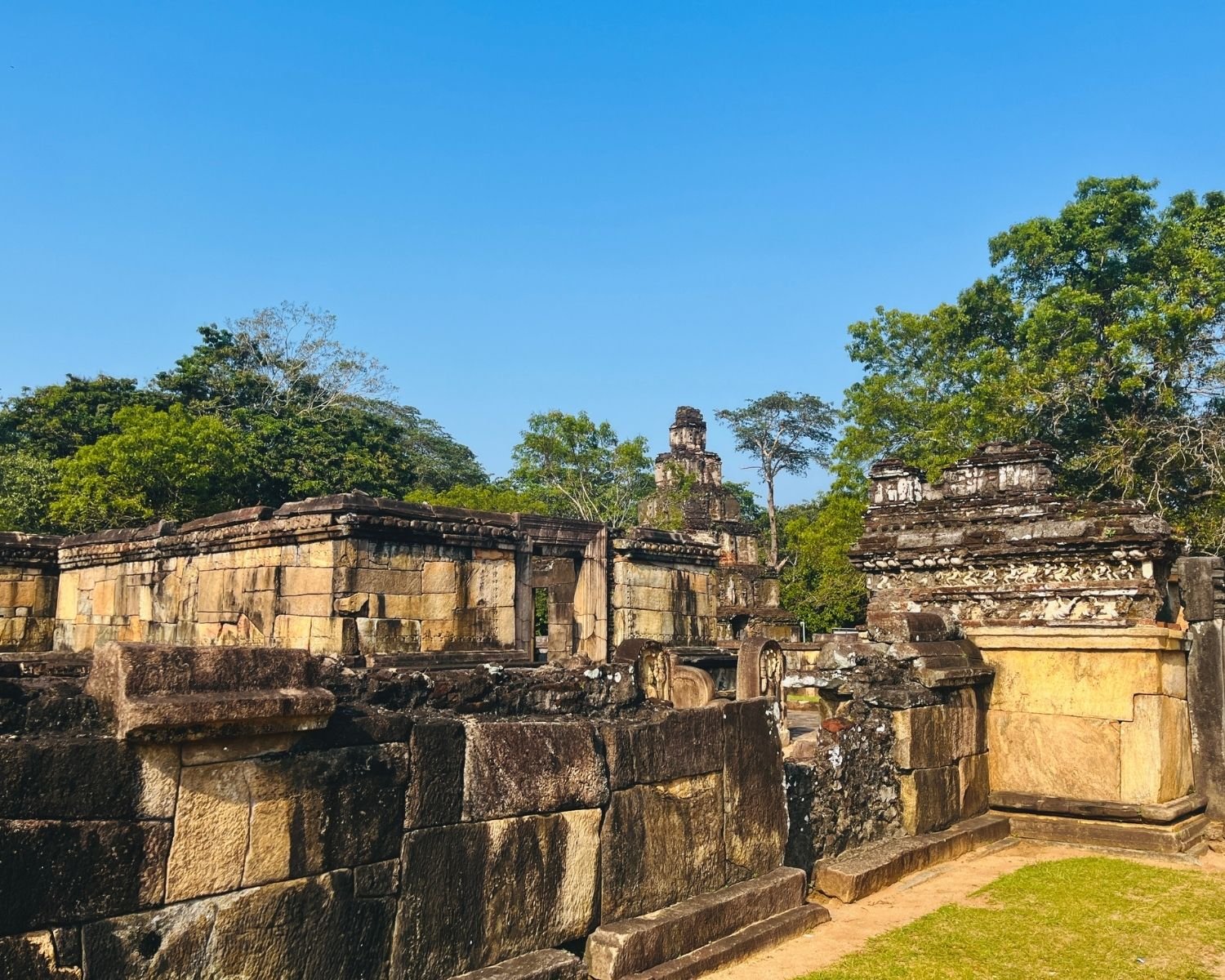 Outer stone enclosure wall of Hatadage with carved frieze, doorway, and Satmahal Prasada tower behind