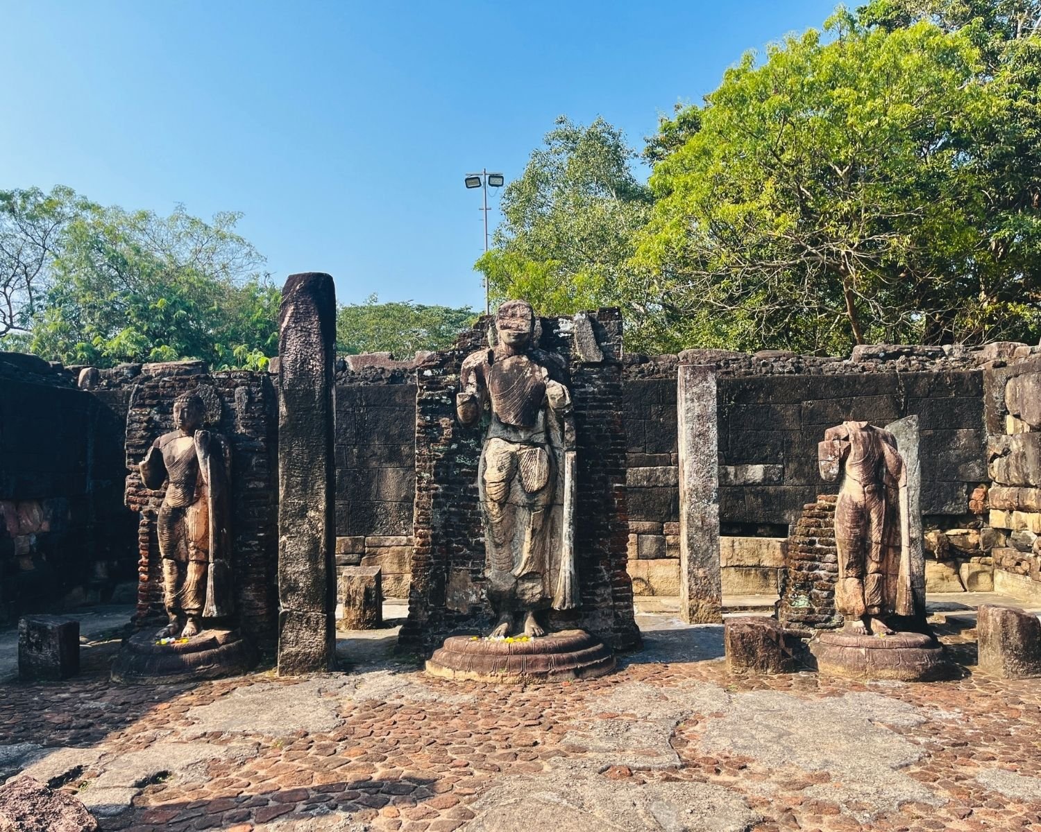 Three standing Buddha statues inside Hatadage ruins with stone pillars and brick walls