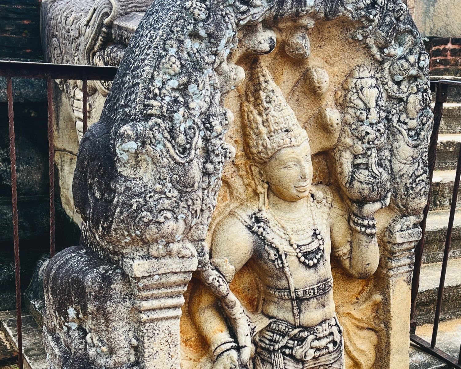 Close-up of Rathna Prasadaya guardstone, Sri Lanka’s most detailed muragala, showing 7th–9th century Nagaraja serpent king holding punkalasa pot of abundance in left hand, under seven-hooded cobra canopy, framed by makara dragon arch with lotuses emerging from its mouth
