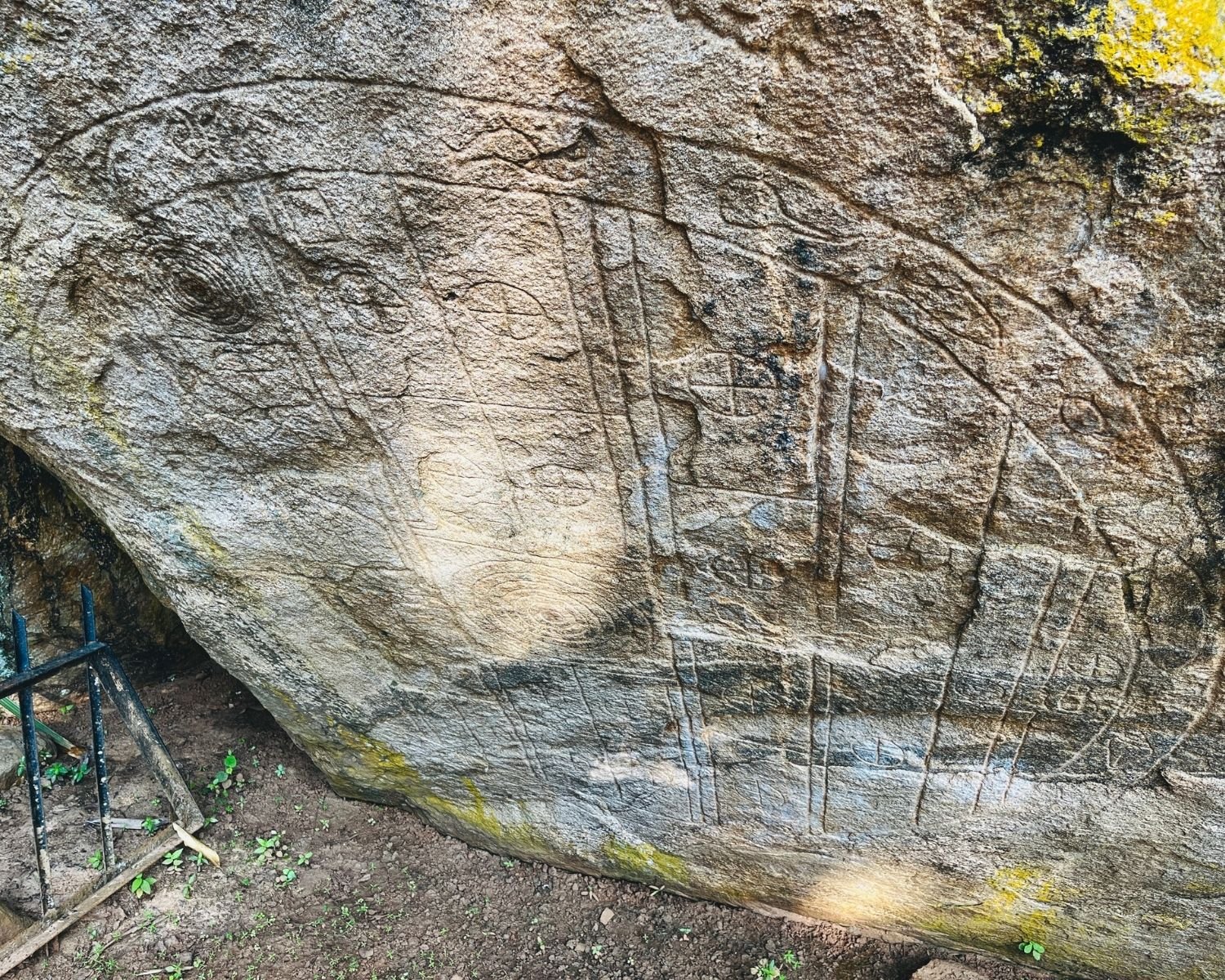 Sakwala Chakraya Stargate ancient rock carving with circular cosmic diagram, concentric circles and symbols etched in black stone with yellow lichen, soil and metal railing near Isurumuniya at Anuradhapura