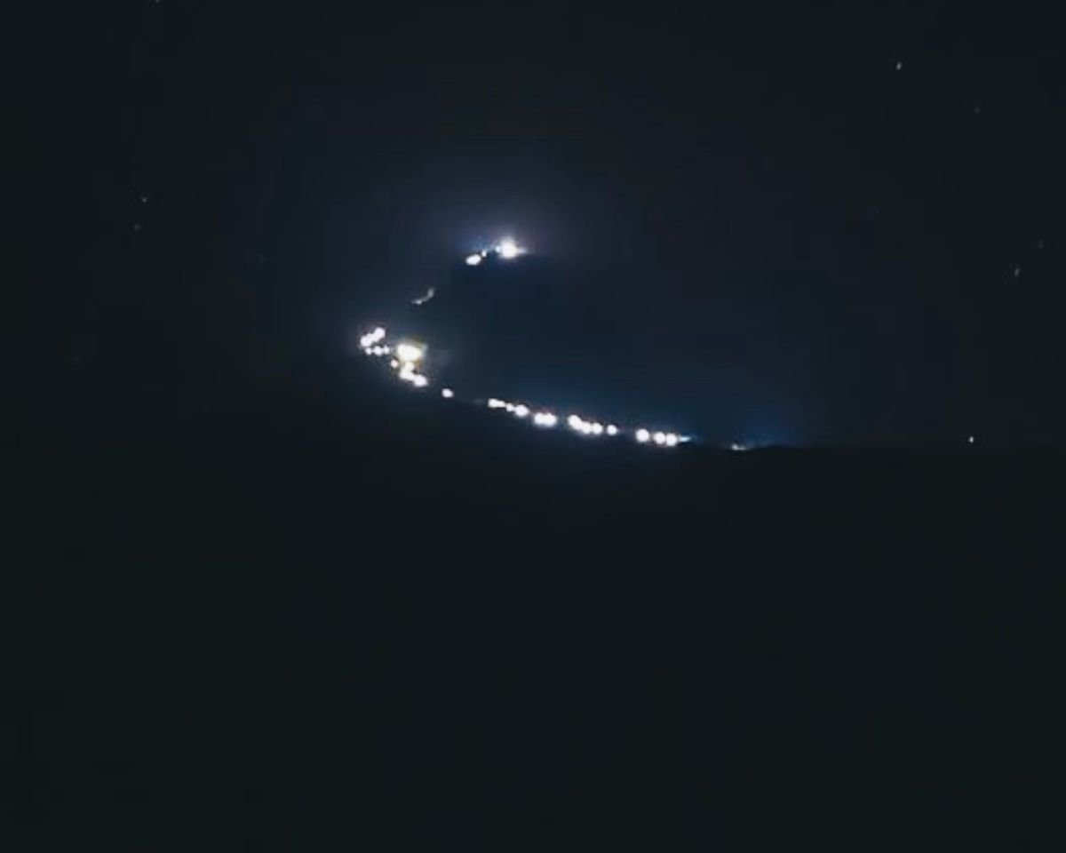 String of lights on Adams Peak Sri Pada pilgrimage trail at night showing summit shrine and Mahagiri Dambe with stars above Peak Wilderness