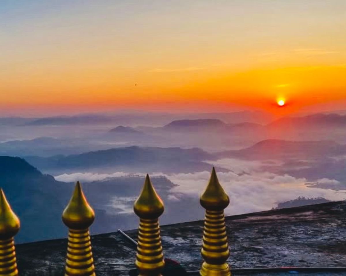 Sunrise above sea of clouds from Adams Peak Sri Pada summit with gold shrine railing in foreground and orange sun over misty Central Highlands