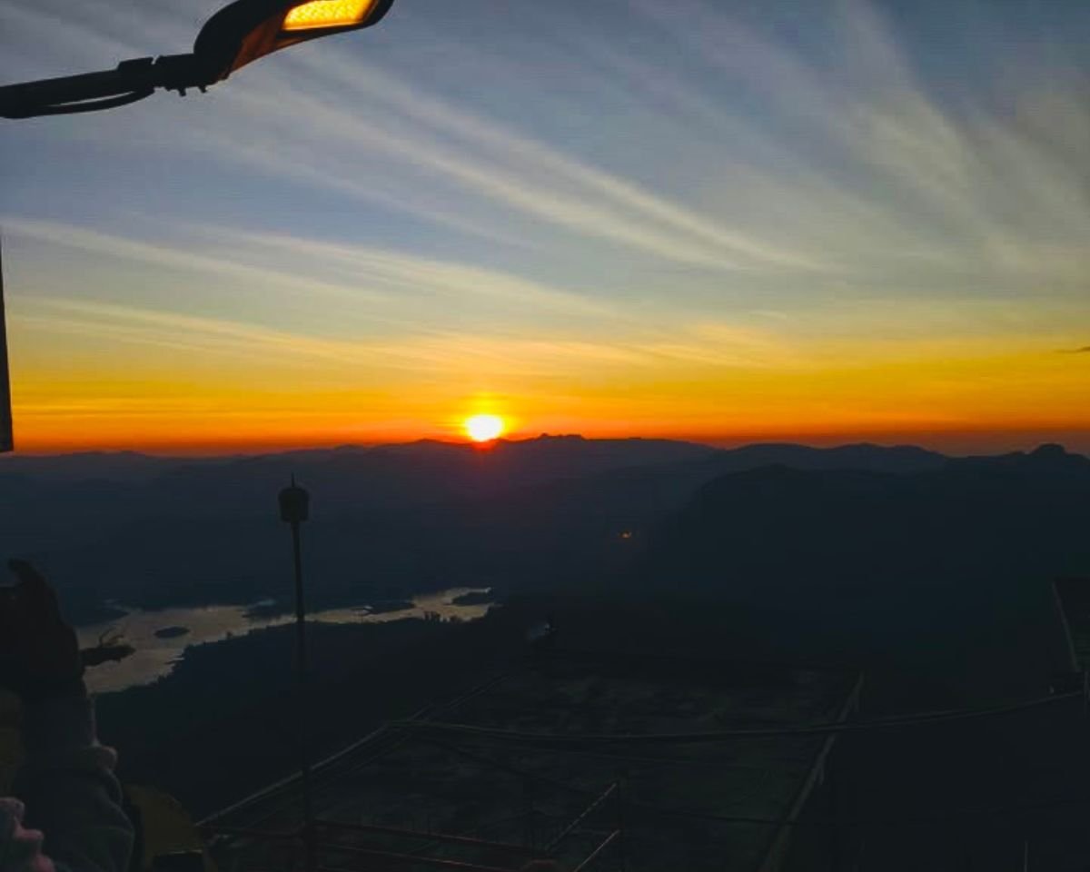 Sunrise from Adams Peak Sri Pada summit over Maussakelle Reservoir with pilgrims on temple deck and layered Central Highlands ridges under orange sky