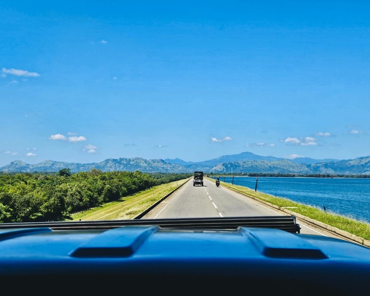 Driving across the Udawalawe Reservoir dam with mountain views in the distance