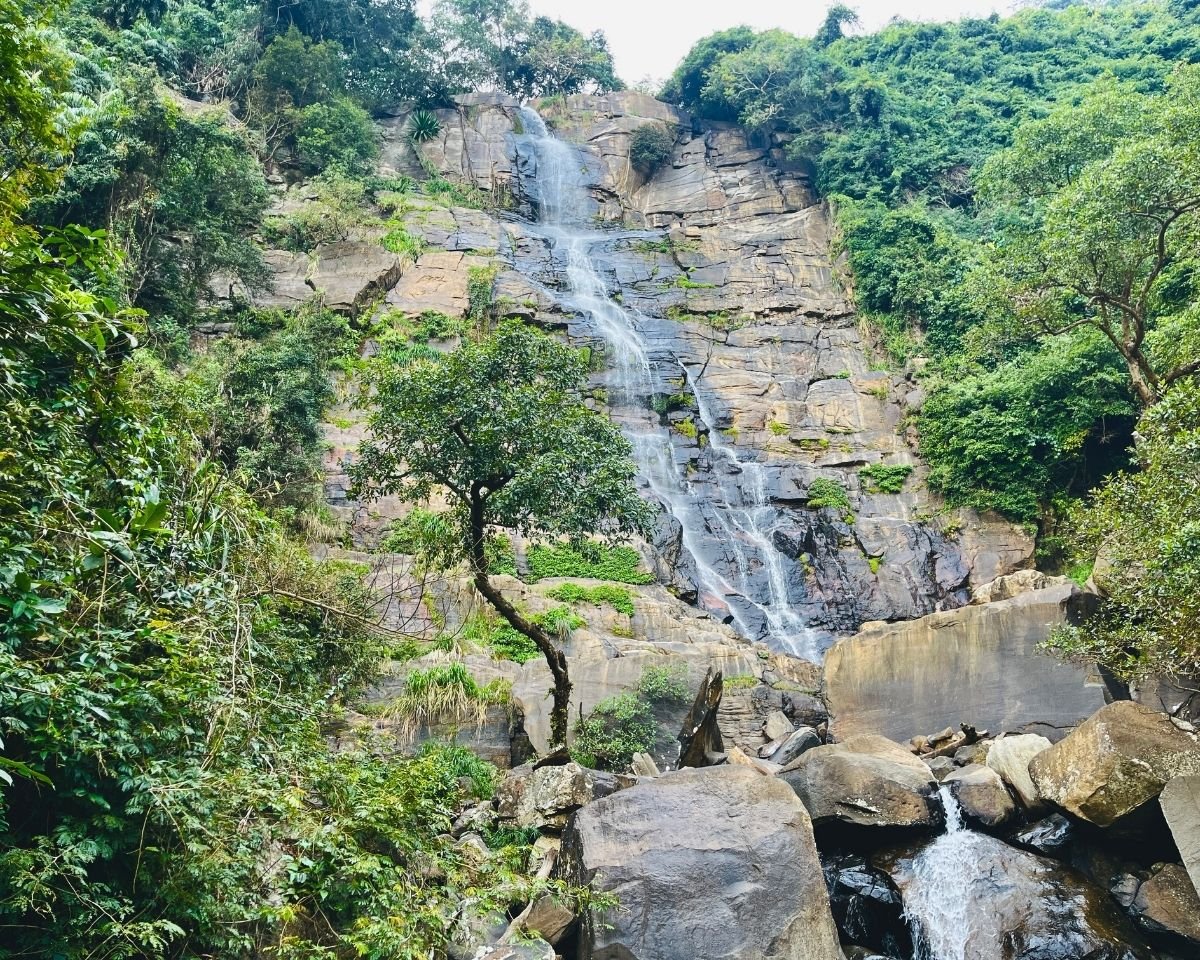 Wisari Waterfall flowing down a layered rock face into a forest stream