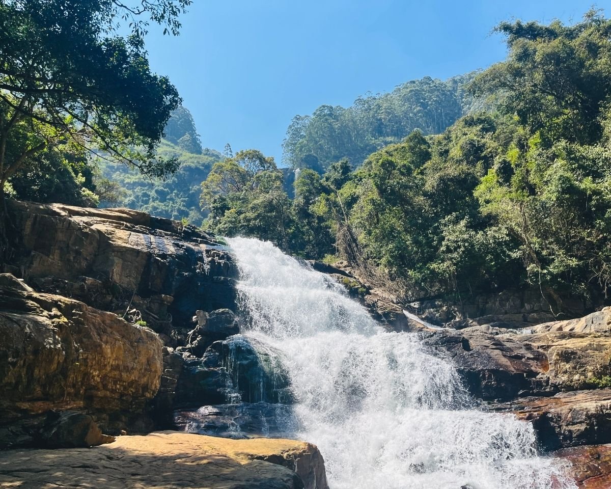 Stepped rock cascade below Bomburuella Waterfall with main falls visible through forest in Nuwara Eliya Sri Lanka