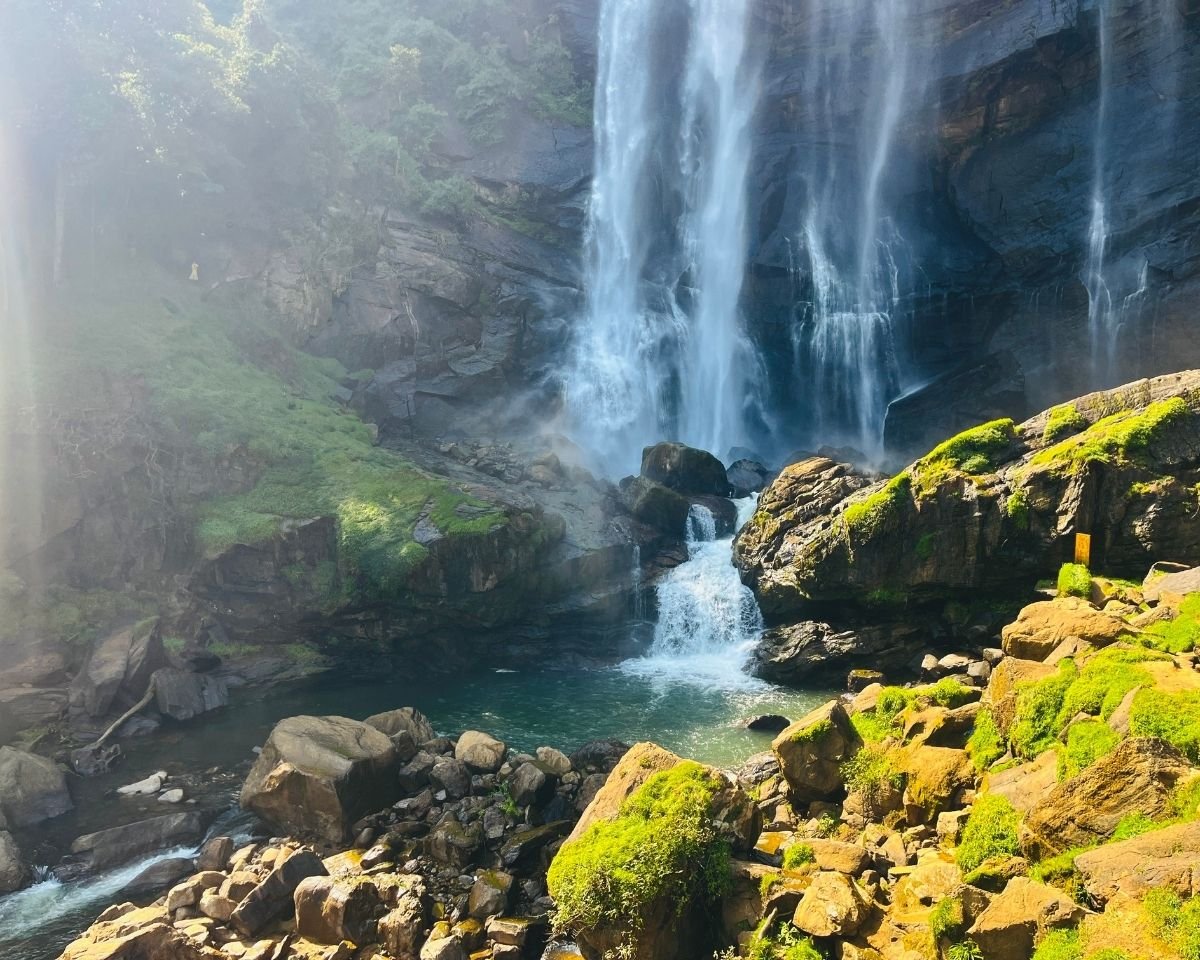 Bomburuella Waterfall main cascade dropping into emerald plunge pool with mist and sunlit moss rocks at base in Nuwara Eliya Sri Lanka