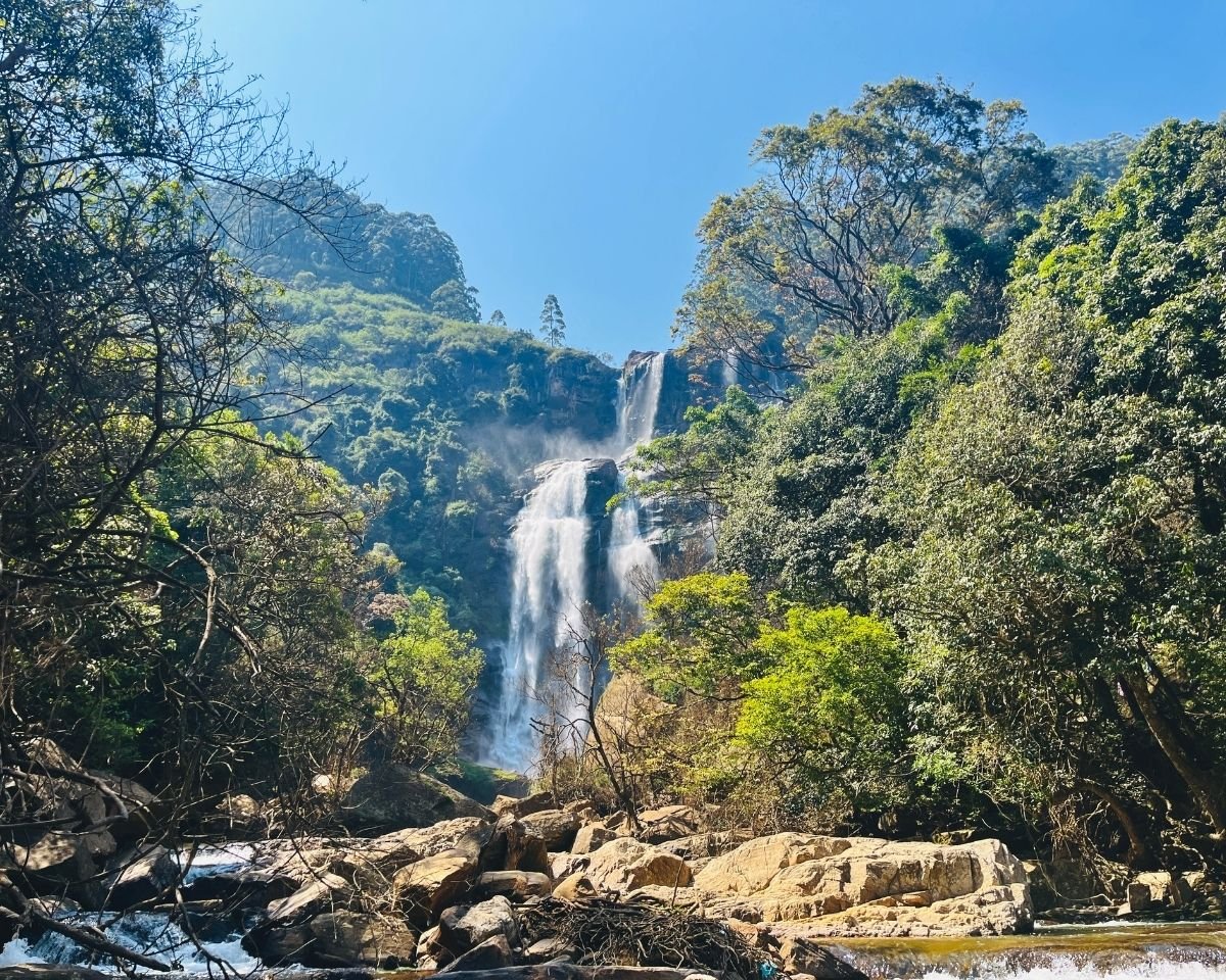 Bomburuella Waterfall seen from rocky spillway channel a few meters in front with sunlit boulders and forest in Nuwara Eliya Sri Lanka
