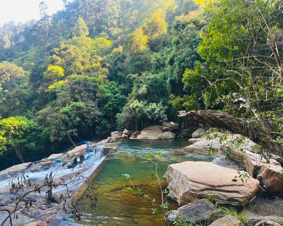 Concrete spillway and emerald pool at the top of Bomburuella Waterfall with flat rocks and forest in Nuwara Eliya Sri Lanka