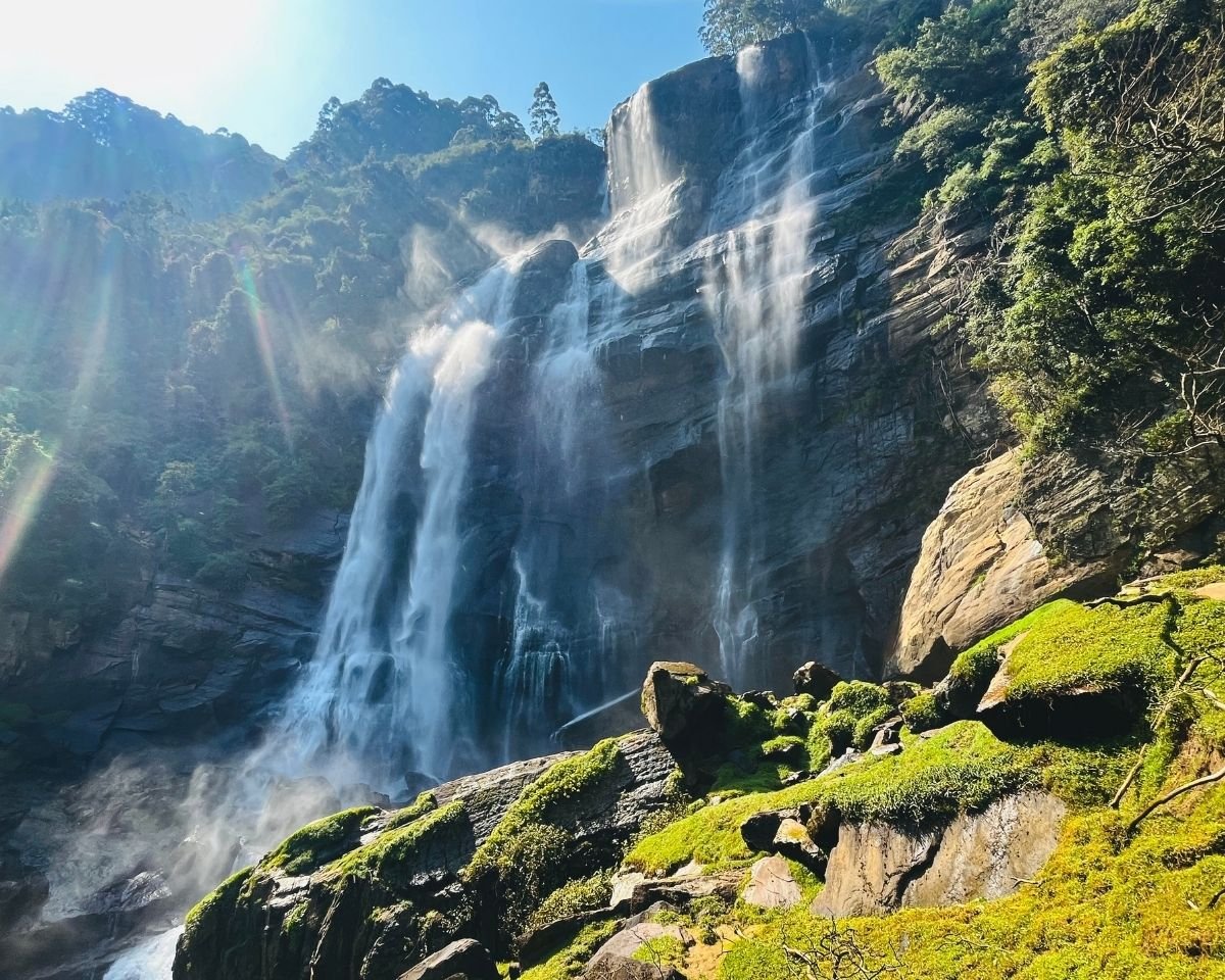 Bomburuella Waterfall twin cascades with sun rays and mist over mossy boulders at base in Nuwara Eliya Sri Lanka