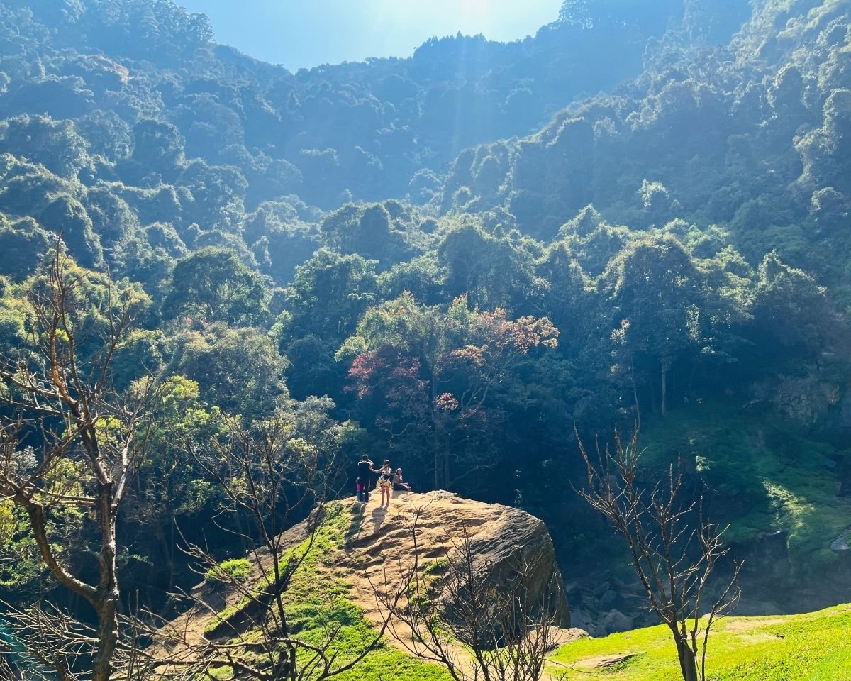 Natural rock watchpoint overlooking forested valley at Bomburuella Waterfall with sun rays through jungle hills in Nuwara Eliya Sri Lanka