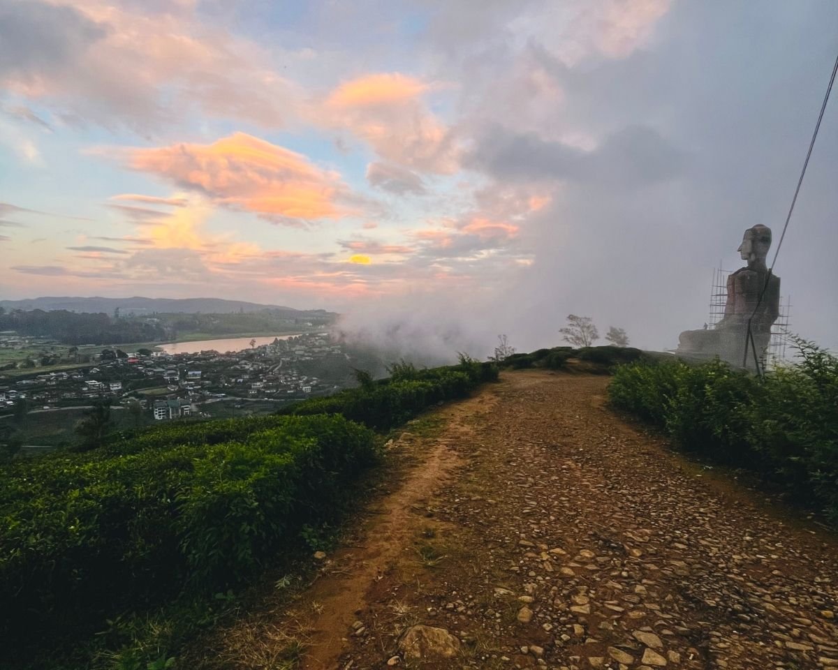 Path to large Buddha statue under construction with Gregory Lake and Nuwara Eliya town at sunset from Single Tree Hill Swarnagiri temple Sri Lanka