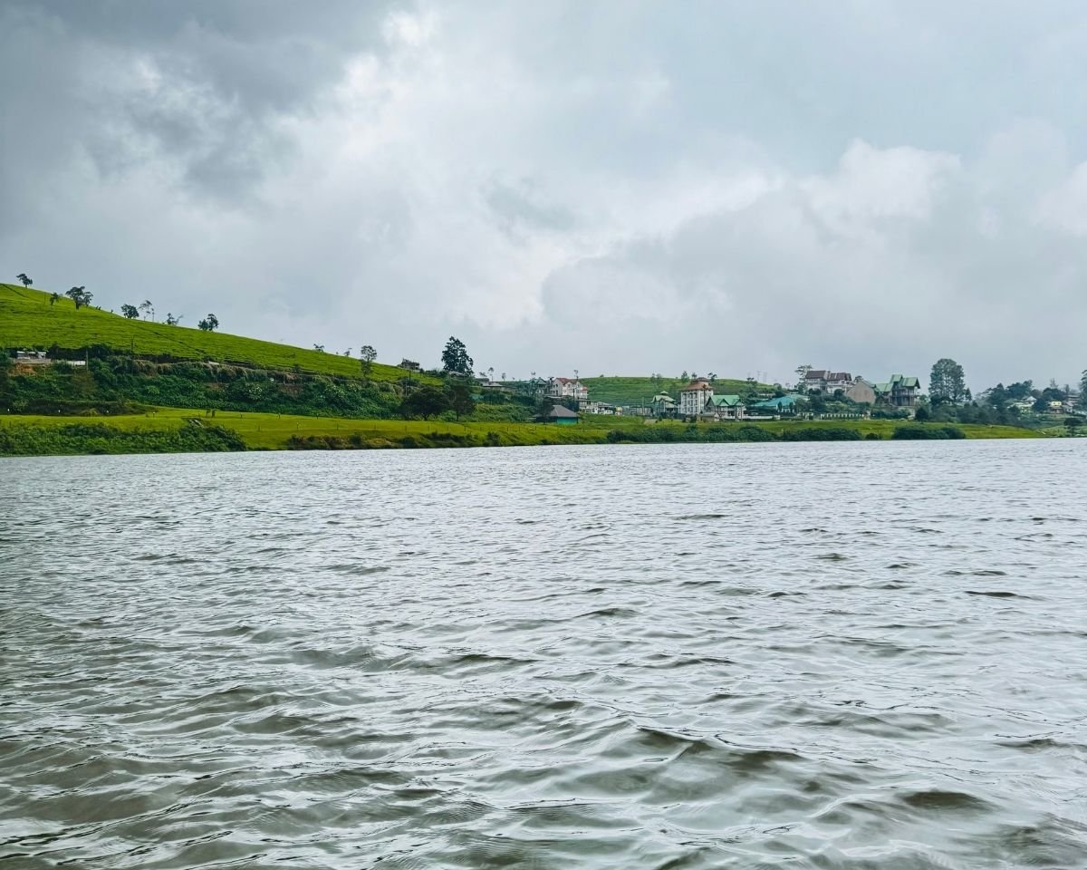 View from boat on Gregory Lake with tea plantation hill and hotels on shore under cloudy sky Nuwara Eliya