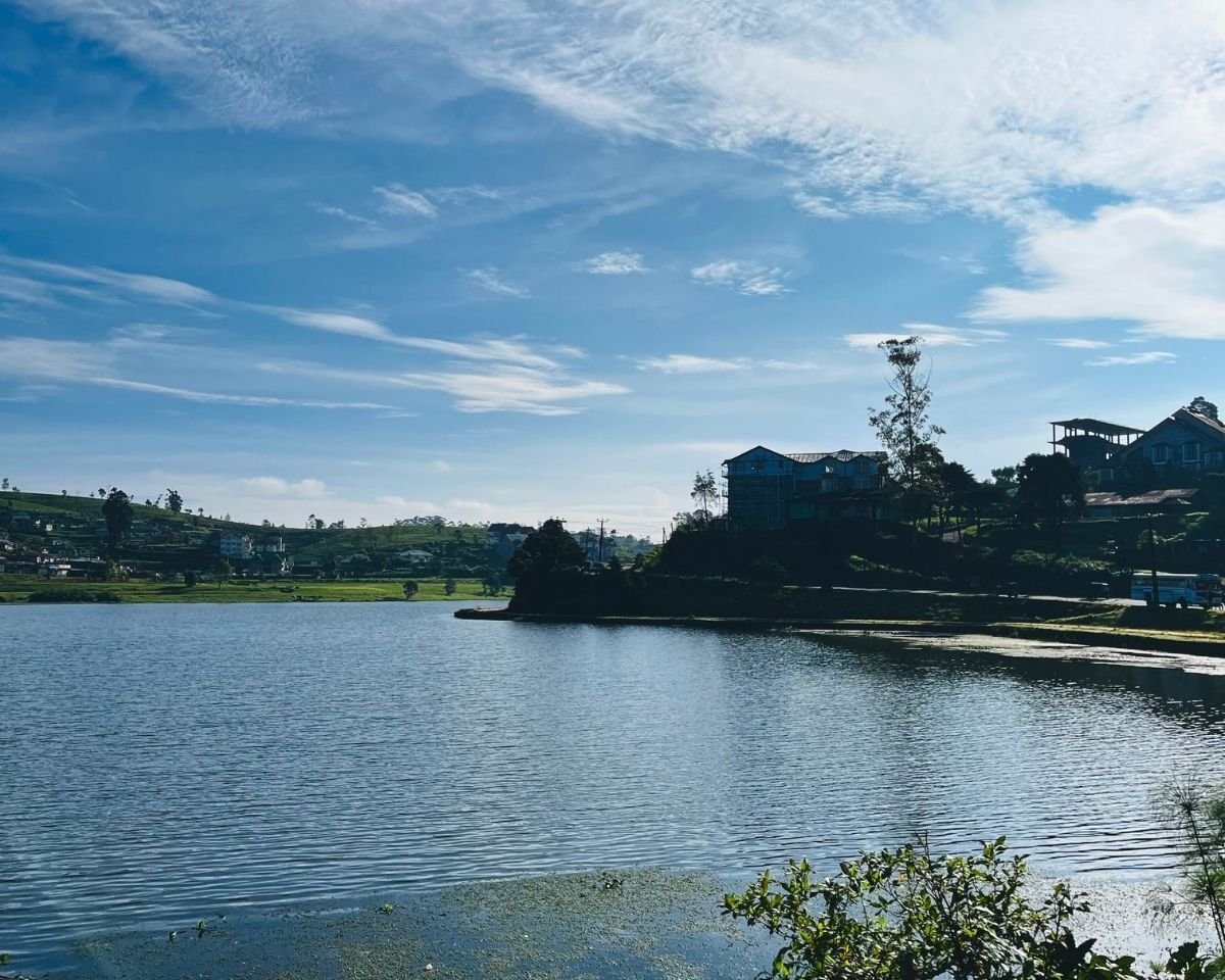 Gregory Lake with clear blue water and European style buildings with tea estates and hills under blue sky in Nuwara Eliya Sri Lanka